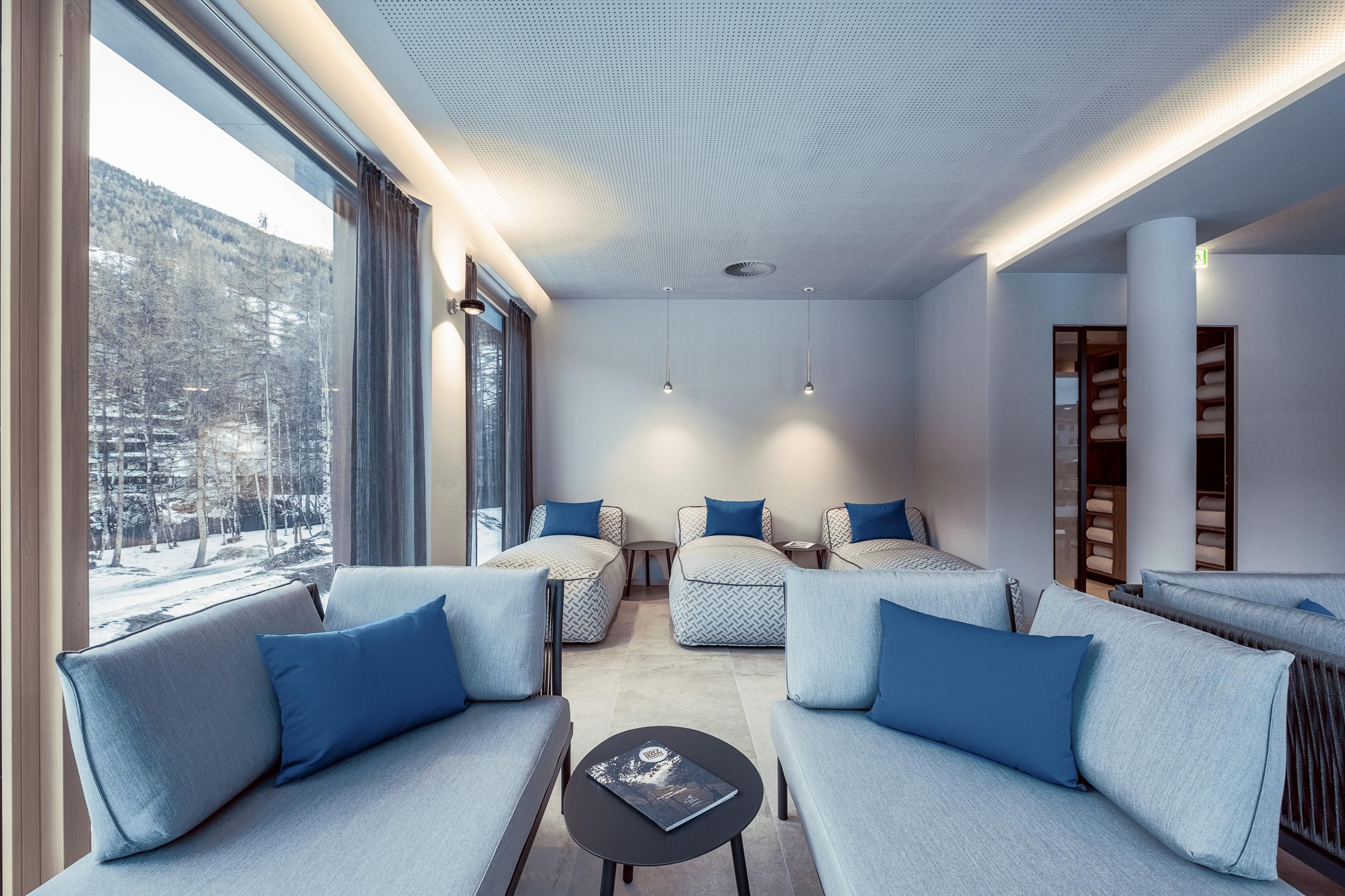 A modern lounge room with bright sofas and blue cushions. Large windows provide a beautiful view of the outdoor landscape.