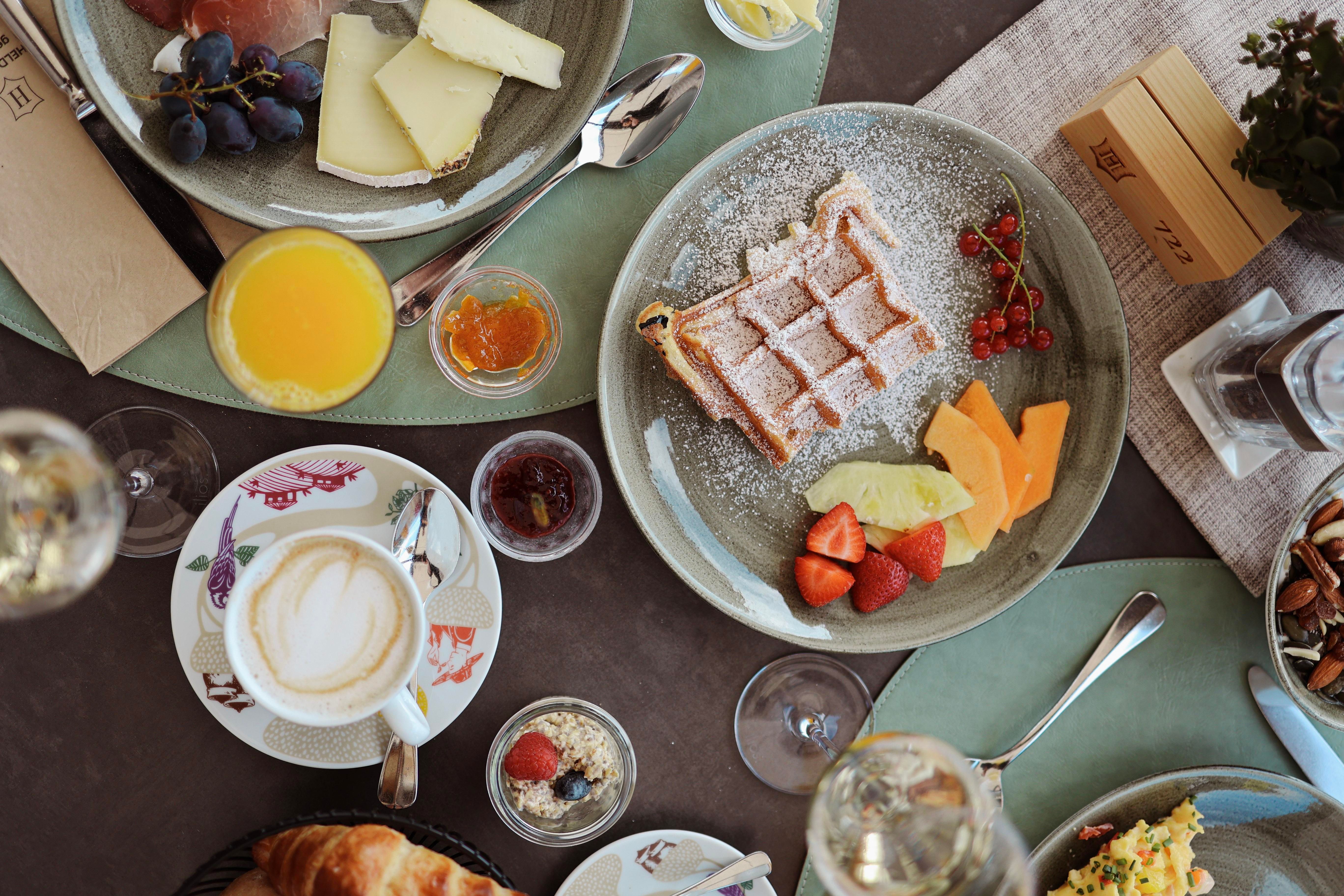 A beautifully set table with various breakfast treats. Featured are waffles, fruits, cheese, croissants, and coffee.