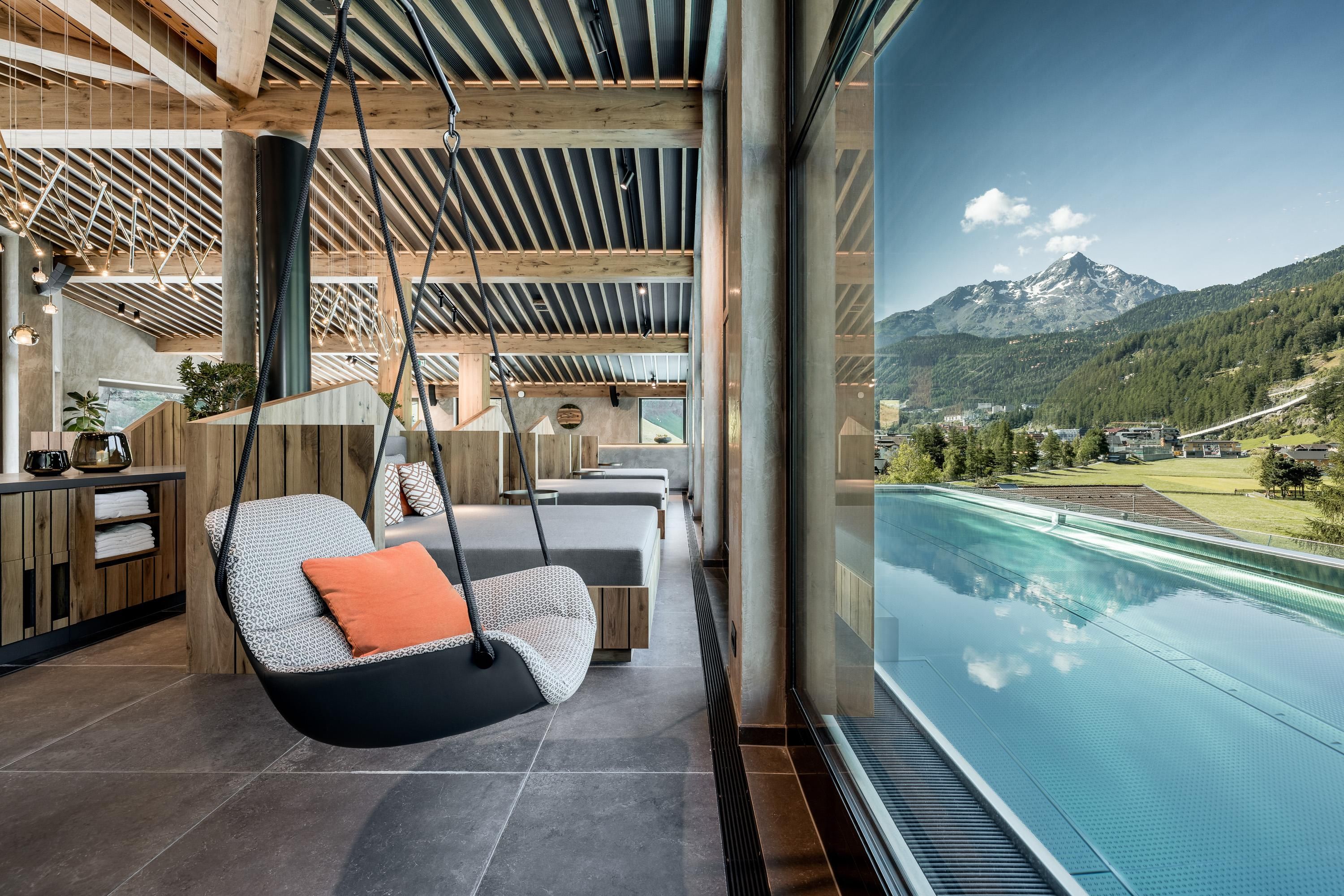 A modern spa with a swinging chair and a view of the mountains. The infinity pool extends to the horizon.