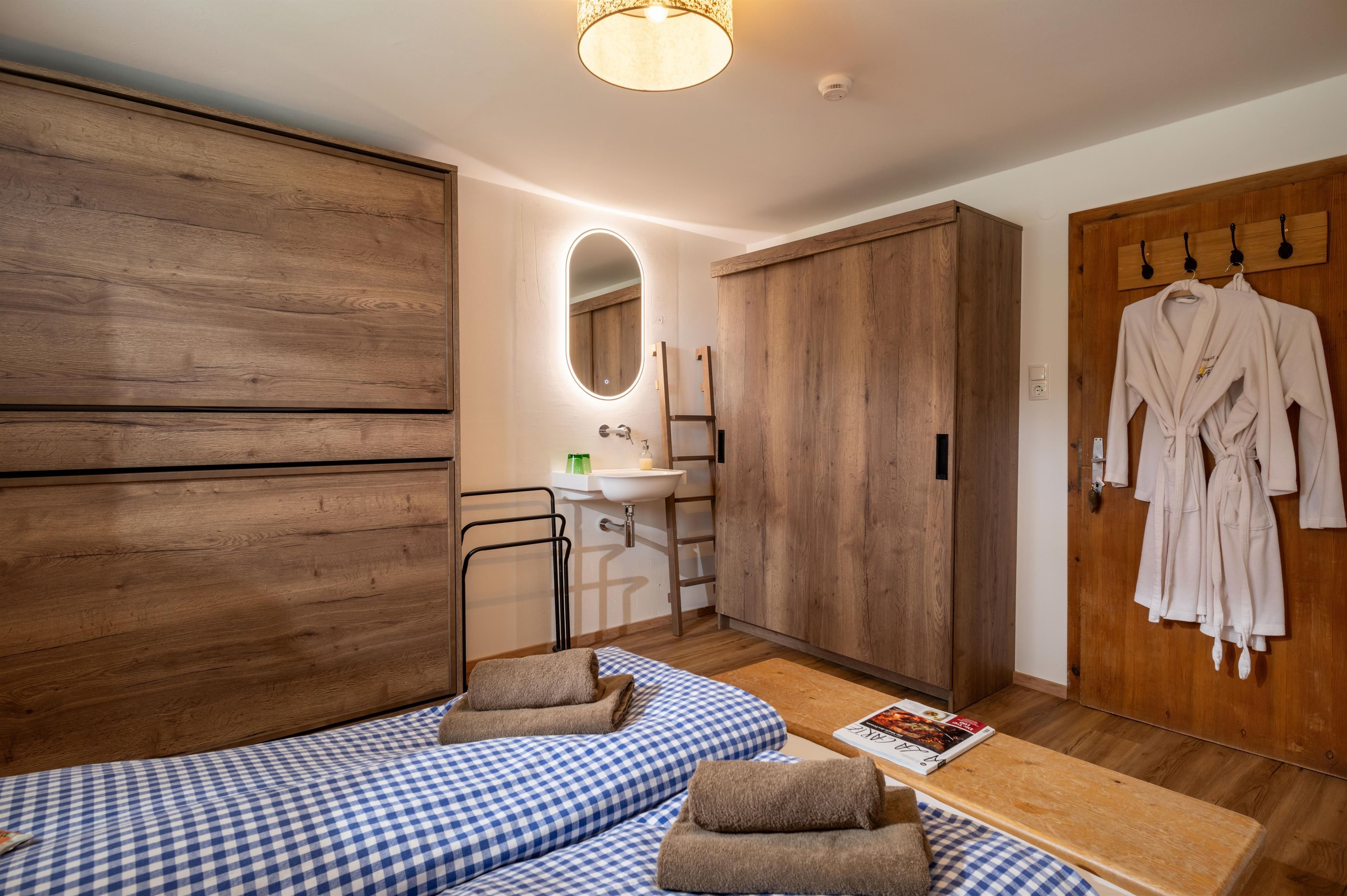 A cozy room with wooden furniture and a large window.Blankets are on the floor and towels are ready for use.