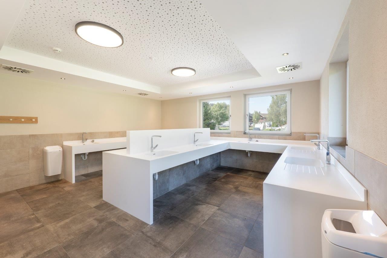 A modern bathroom with white sinks and generous mirrors. Large windows provide plenty of natural light.