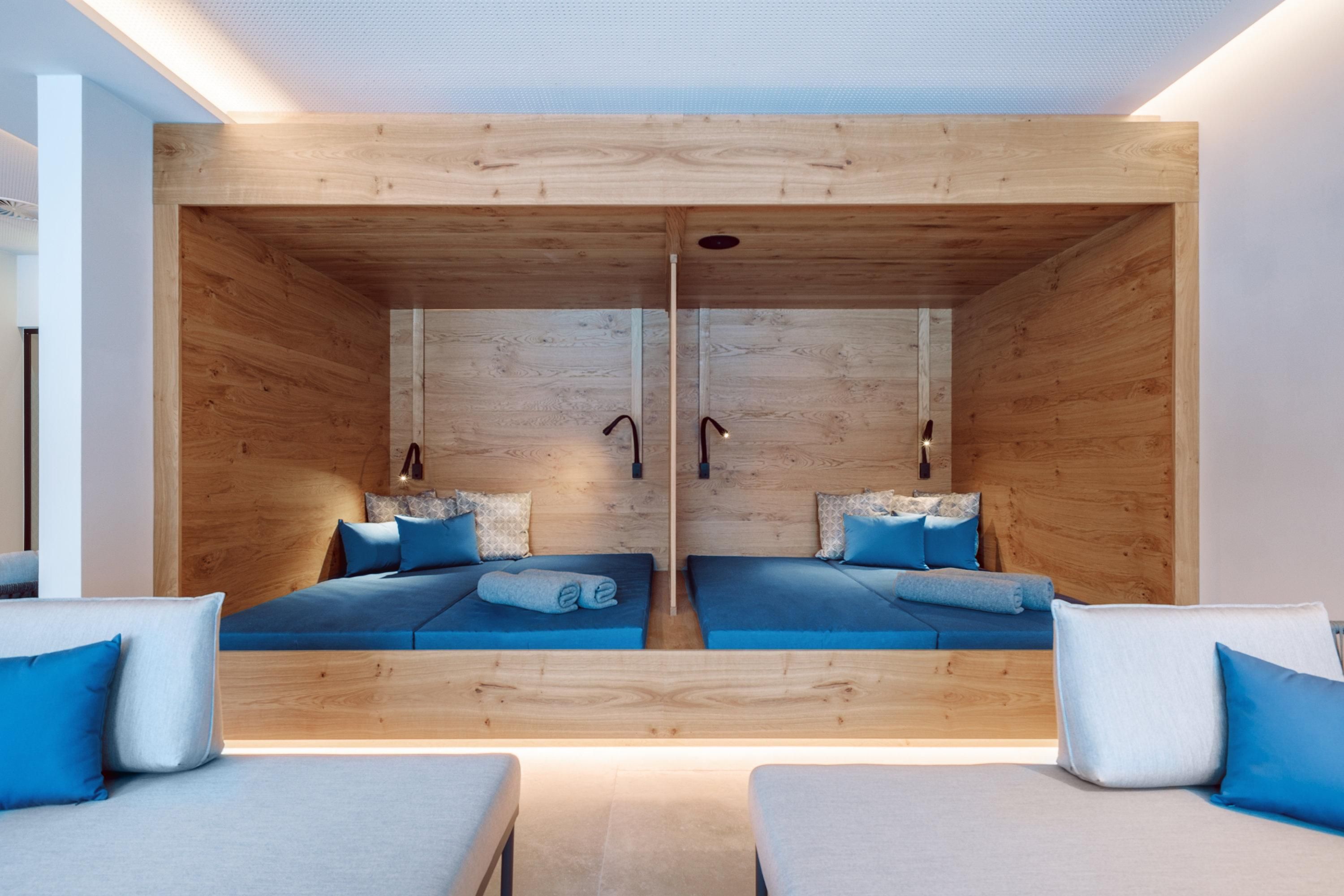A modern bedroom with wooden walls and two beds. The decor is simple and elegant, with blue accents.