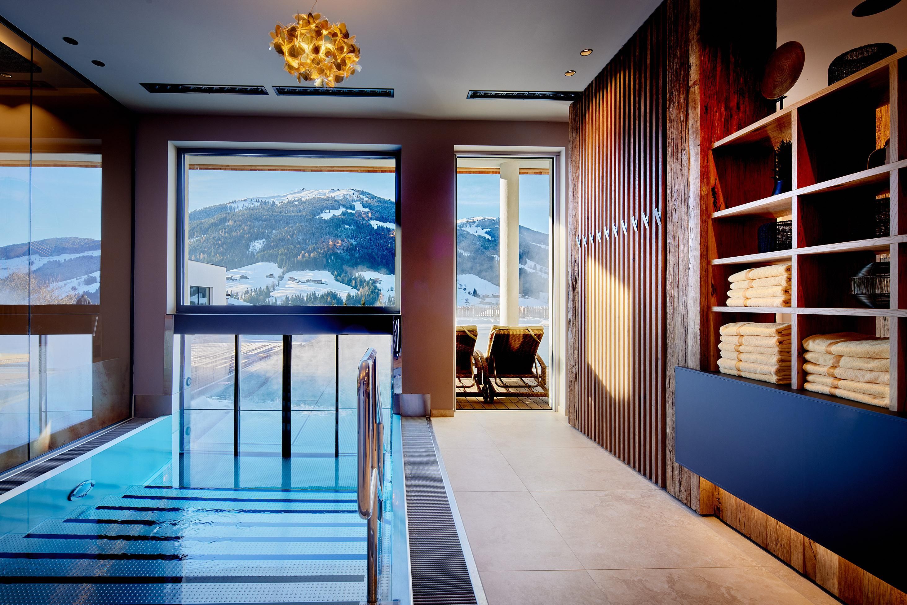 An elegant wellness area with an indoor pool and mountain views. The warm atmosphere is enhanced by large windows and stylish furnishings.