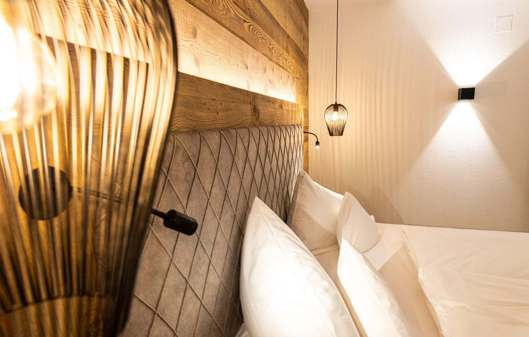 A stylish bedroom with a wooden headboard and soft lighting. The white pillows and modern lamps create a cozy atmosphere.