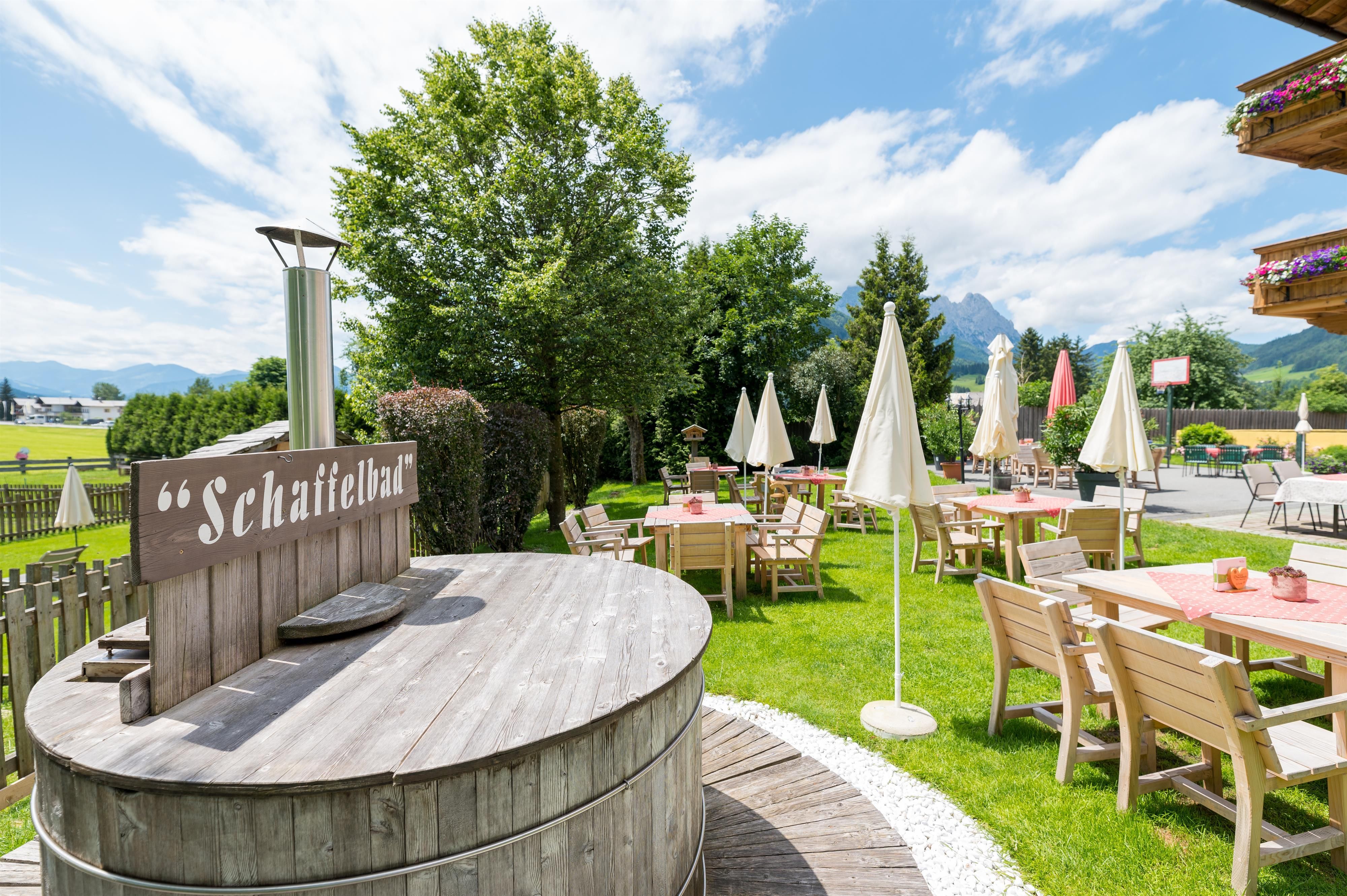 An inviting outdoor area with wooden tables and sun umbrellas. In the background, there are trees and a beautiful mountain landscape.