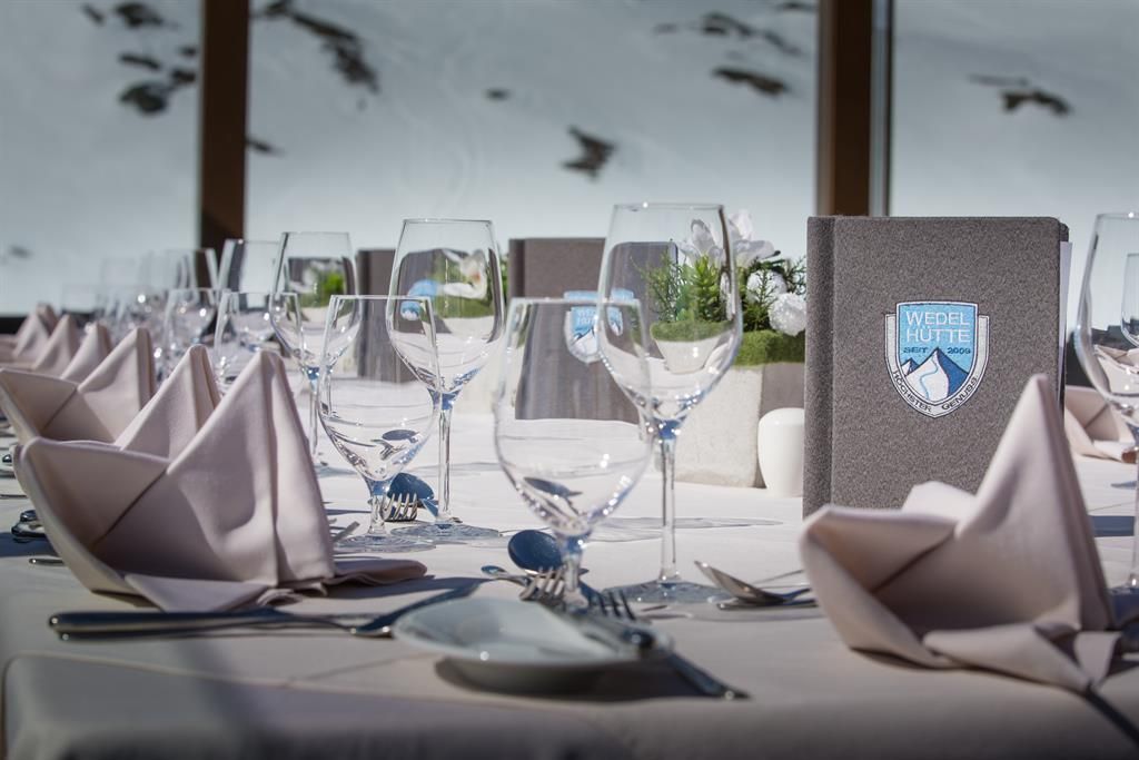 An elegantly set table with glasses, cutlery, and decorative napkins. In the background, snow-covered mountains can be seen.