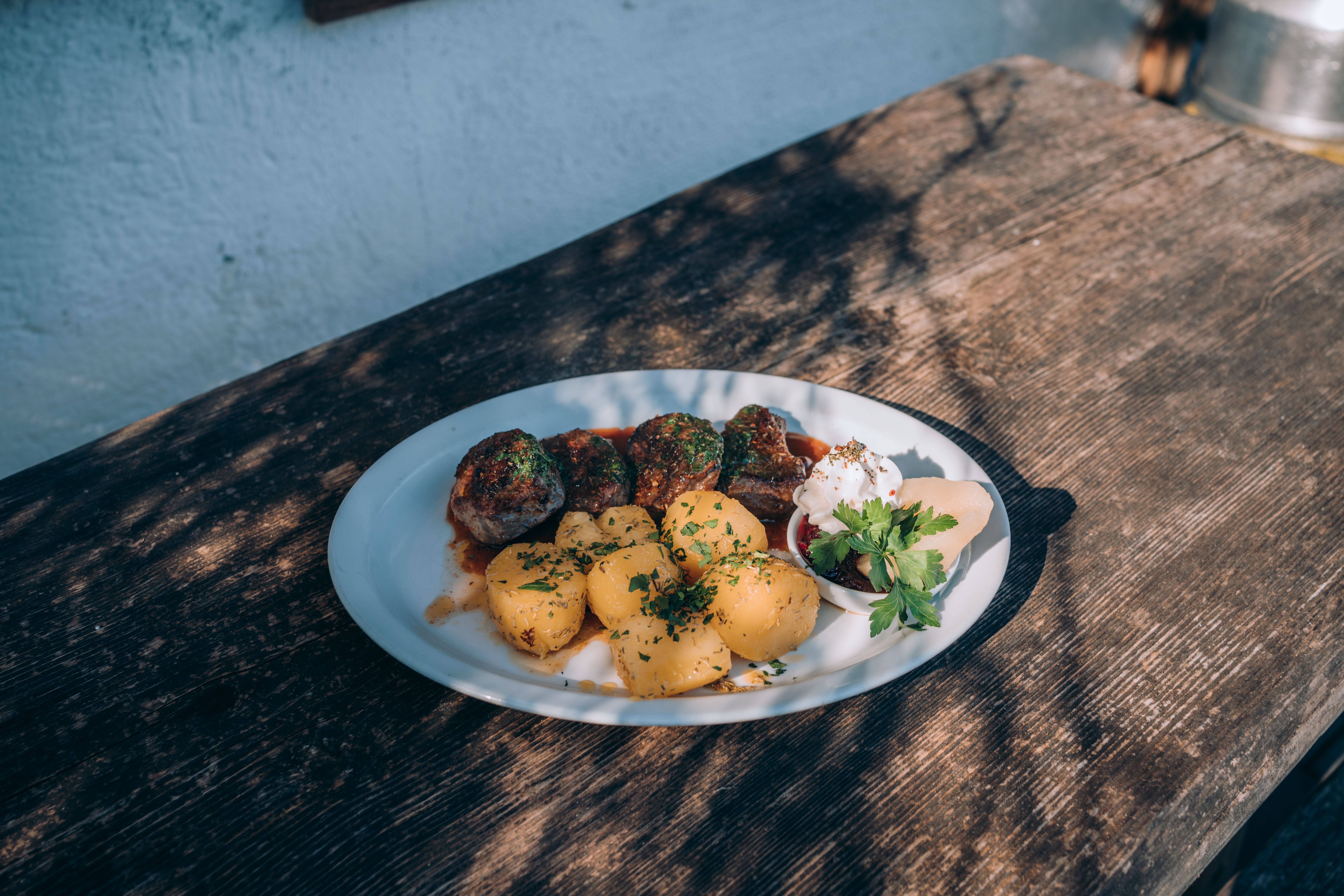 Wildbret auf der Fischbachalm, Teller mit Fleisch und Kartoffeln auf einem Holztisch