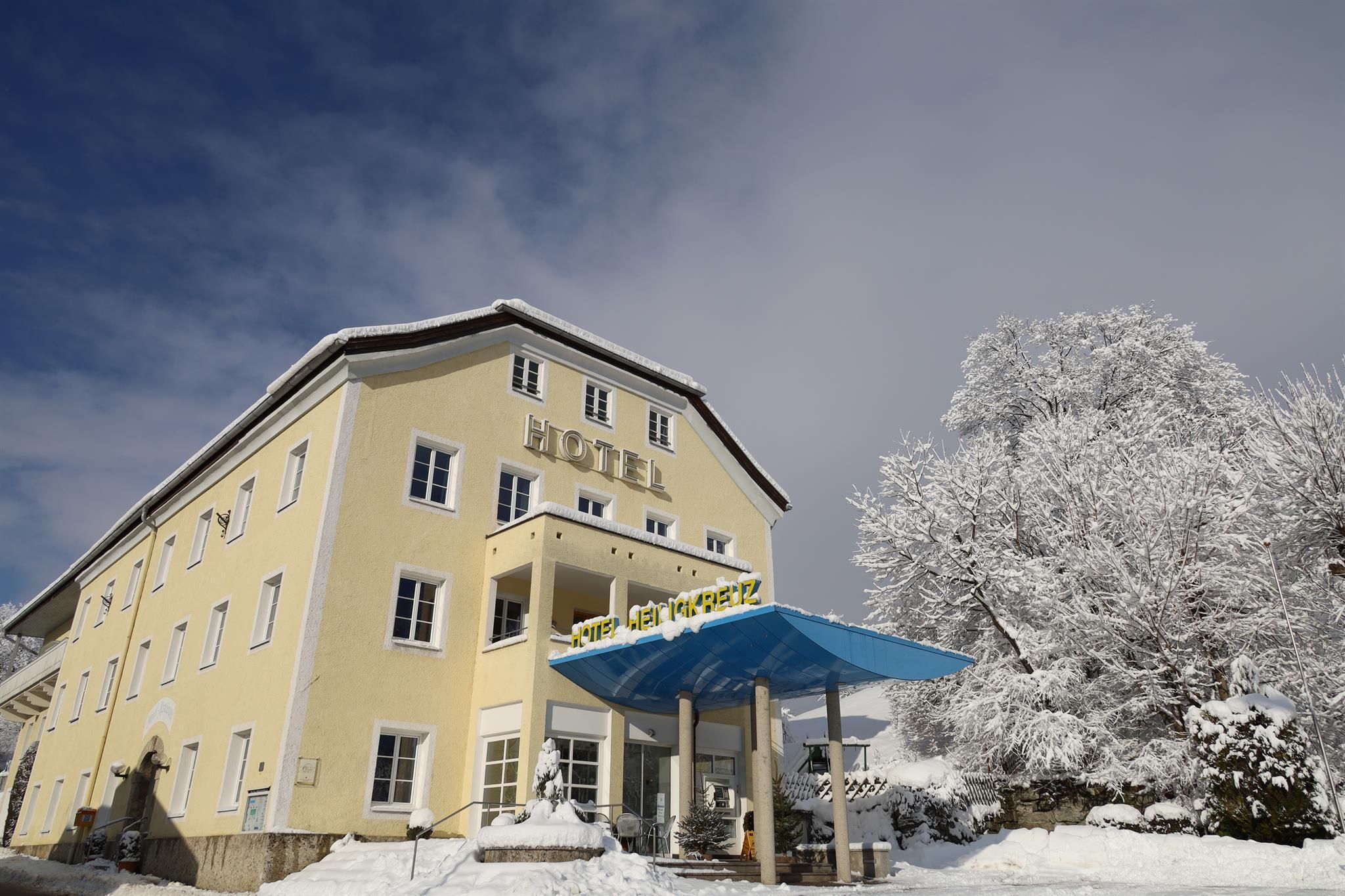 A yellow hotel building in the snow with a blue canopy at the entrance. Surrounded by snow-covered trees and clear sky.