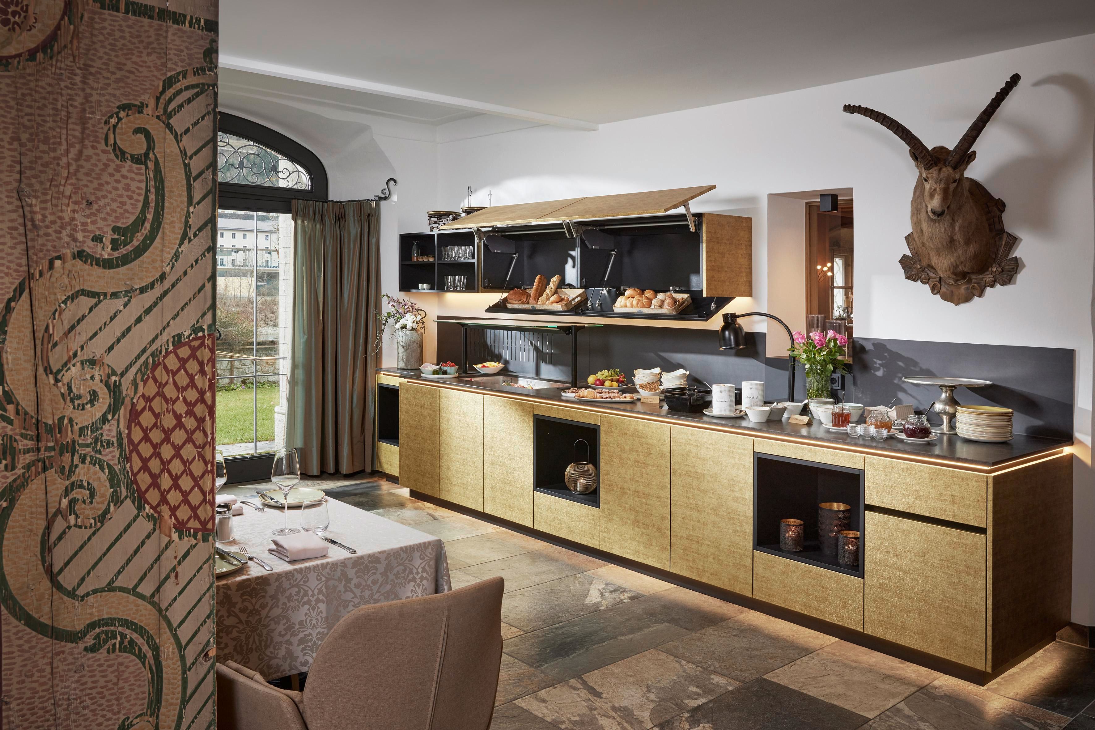 A modern dining room with an elegant breakfast bar. The open kitchen displays various groceries and is furnished with stylish furniture.