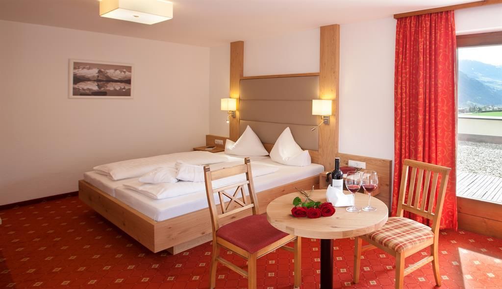 A cozy hotel room with a double bed and a dining table. Large windows offer a beautiful view of the landscape.