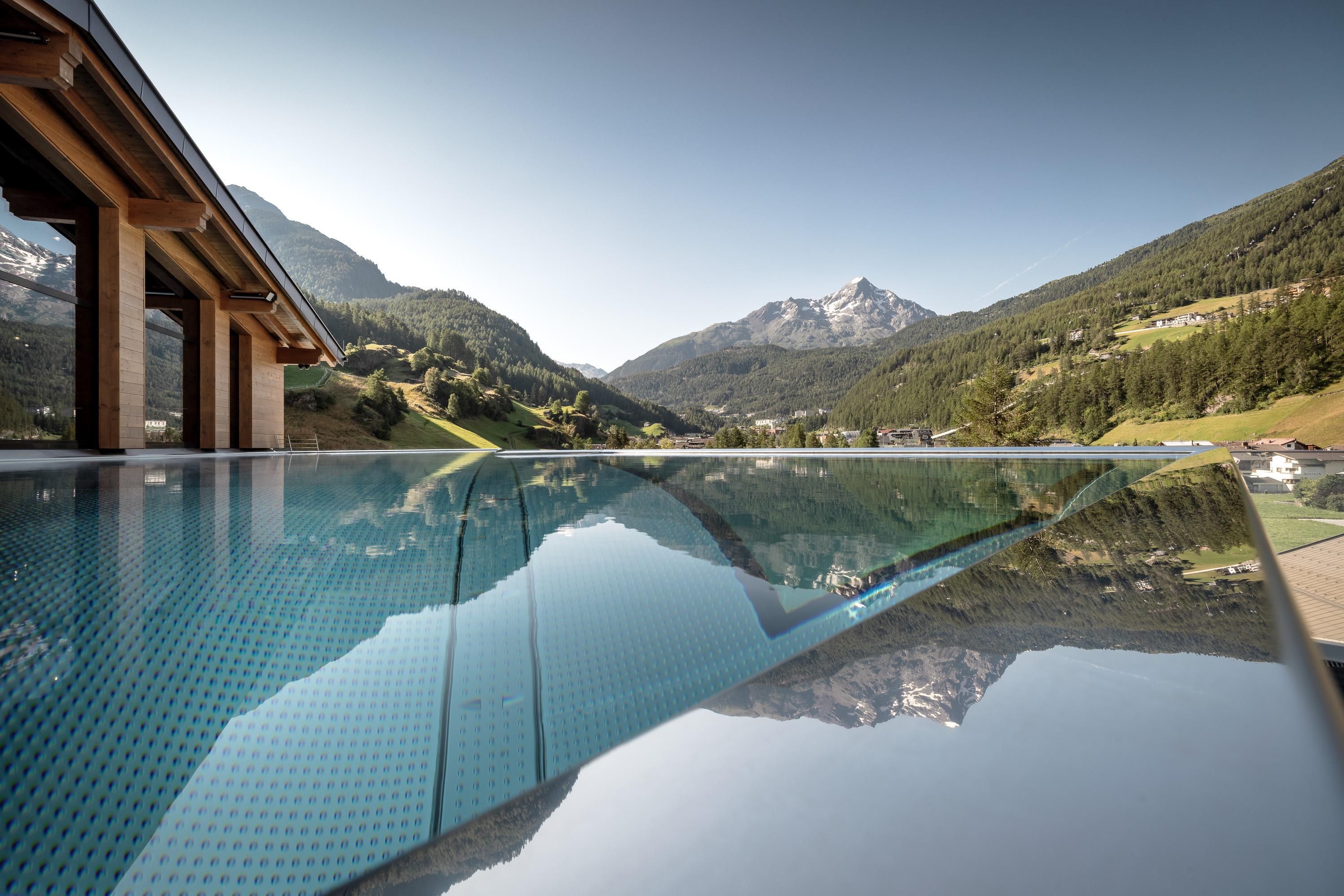An infinity pool with a view of the majestic mountains. The clear water surface reflects the surrounding landscape.
