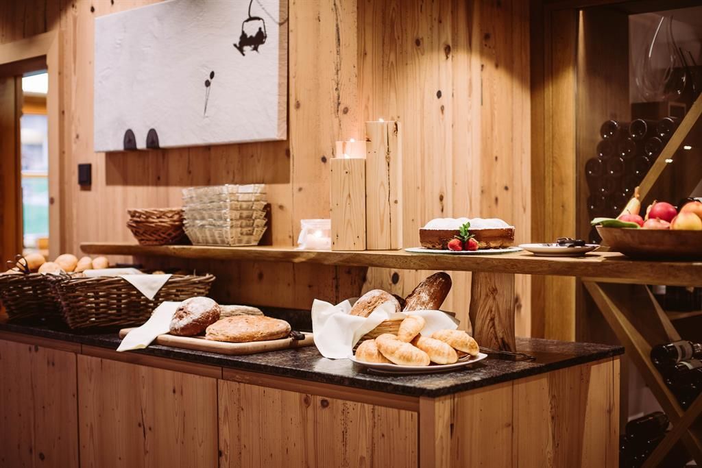 A beautiful dining area with different types of bread on a wooden counter. In the background, there are baskets with rolls and fruits.