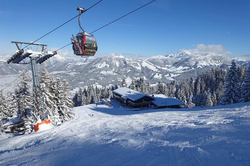 A picturesque winter landscape with snow-covered mountains and pine trees. A gondola glides over the snowy slope.
