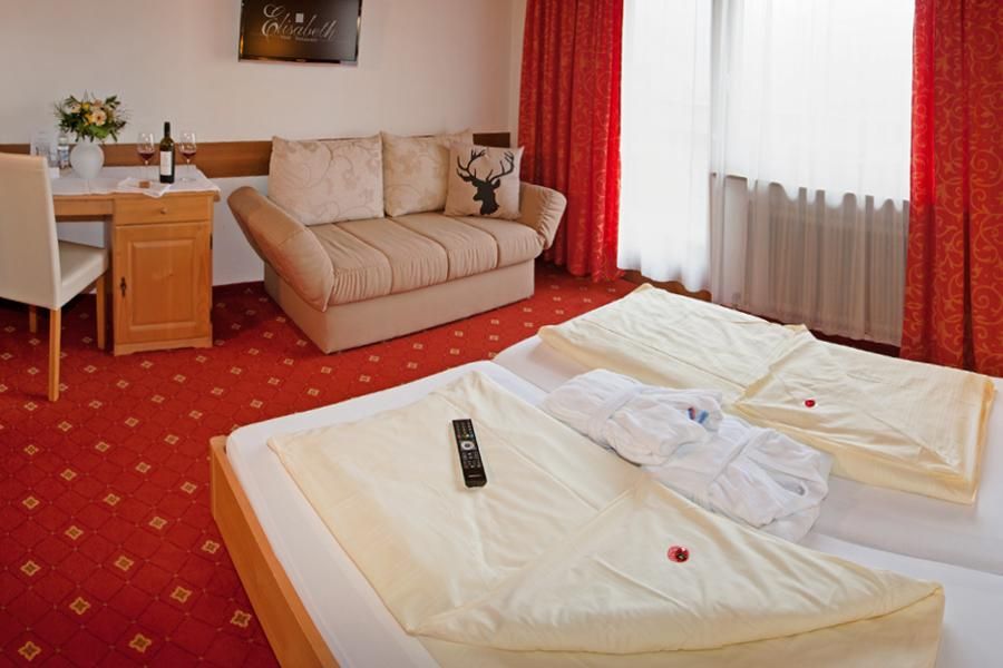 A cozy hotel room with two beds and a couch. The room is furnished with a red carpet and colorful curtains.