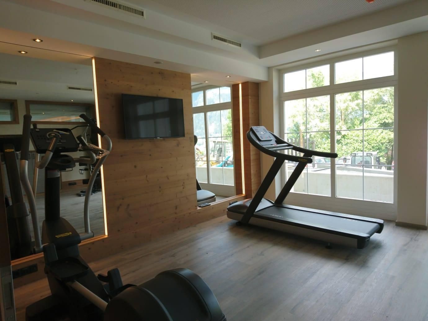 A modern gym with a treadmill and a cable machine. Large windows provide plenty of daylight and a pleasant atmosphere.