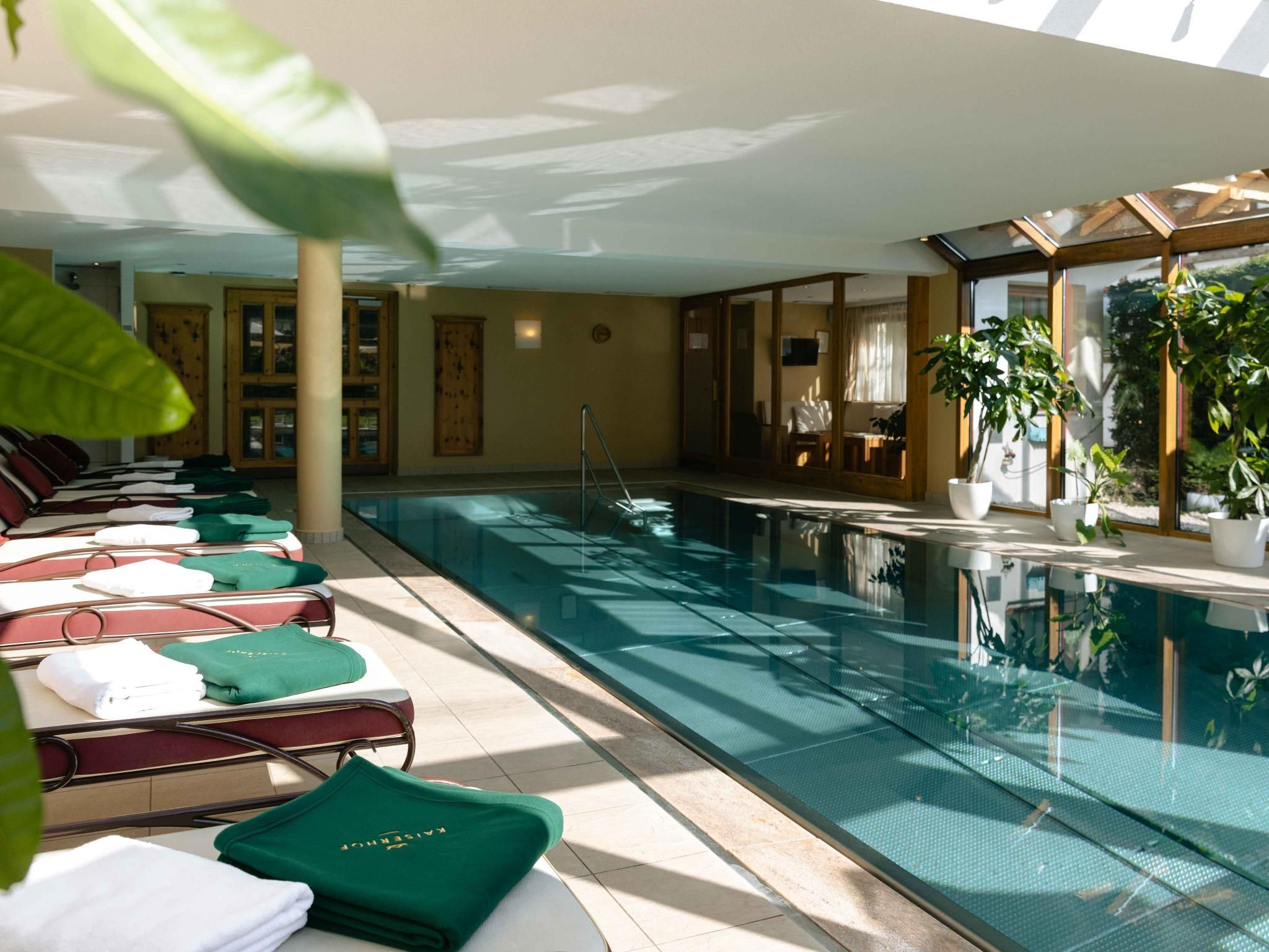 An elegant indoor area with a glass pool and loungers. Lush plants create a relaxed atmosphere.