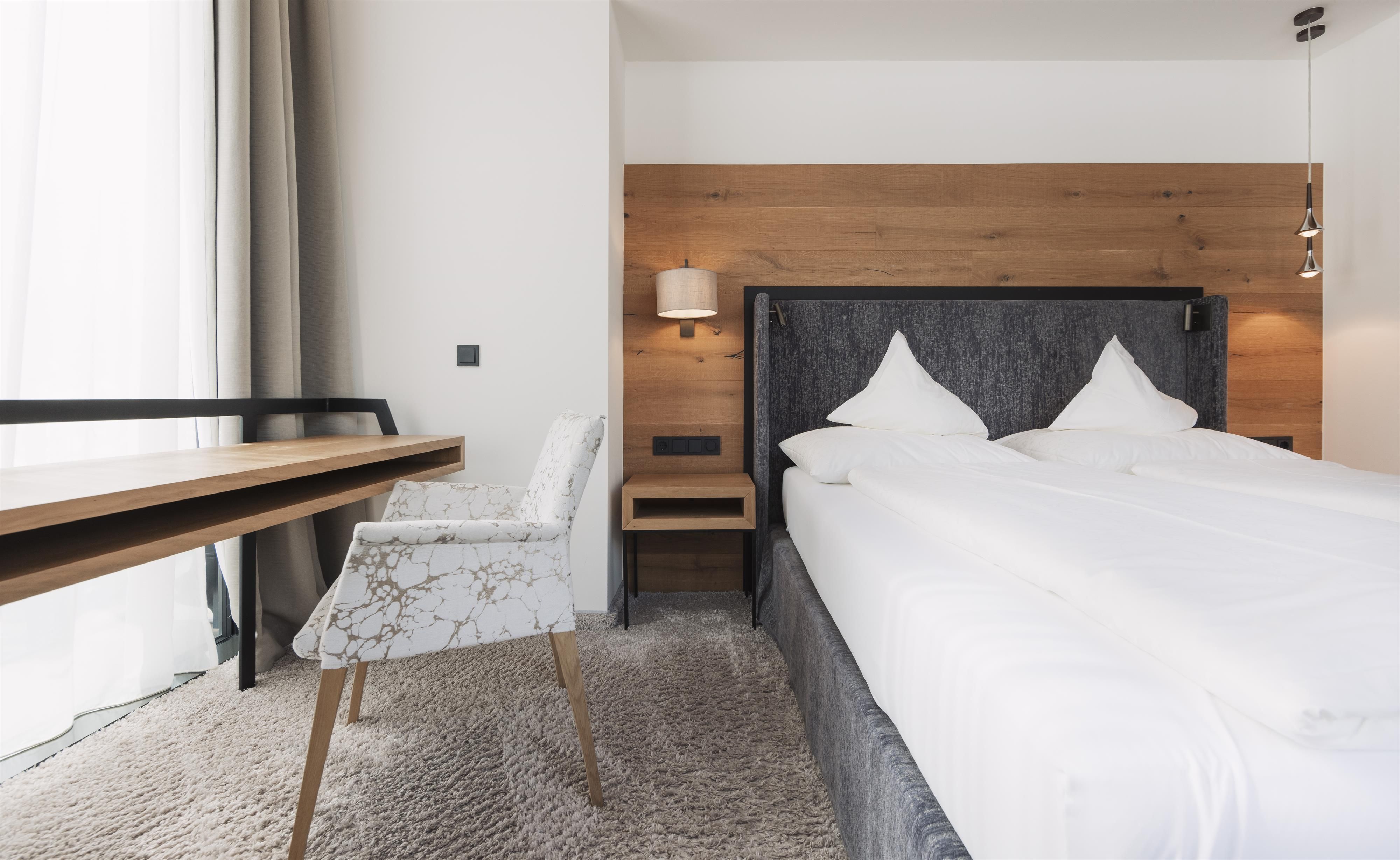 A modern bedroom with a large bed and an elegant chair. Soft colors and plenty of light create an inviting atmosphere.