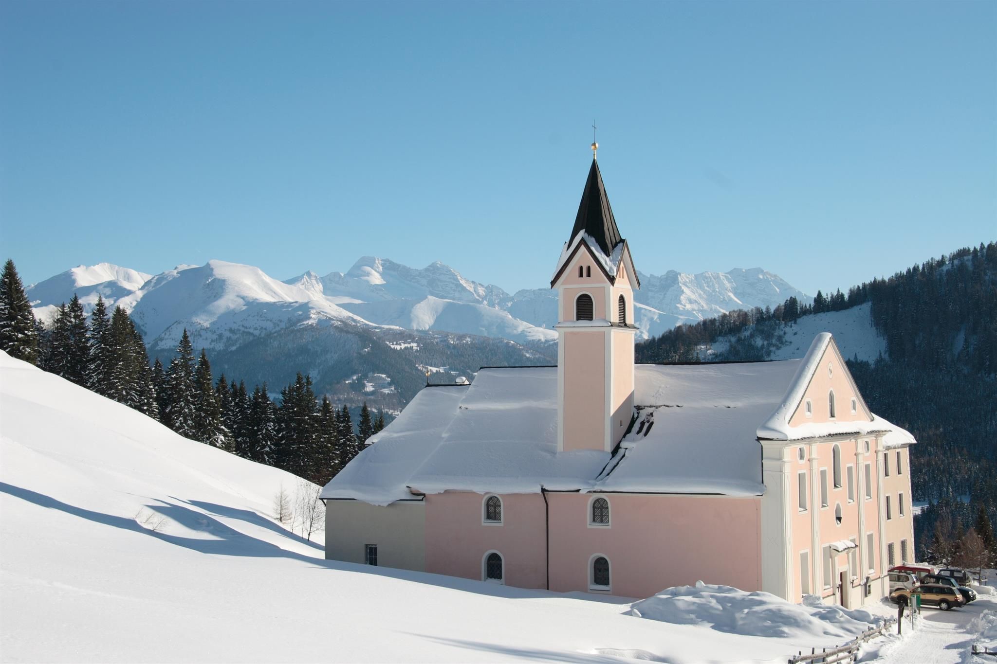 A picturesque church in a snow-covered landscape. In the background, majestic mountains and a clear blue sky can be seen.