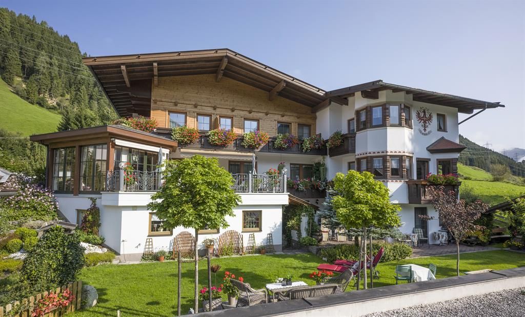 A charming alpine house with a beautiful garden. In the background, green mountains and a clear sky can be seen.