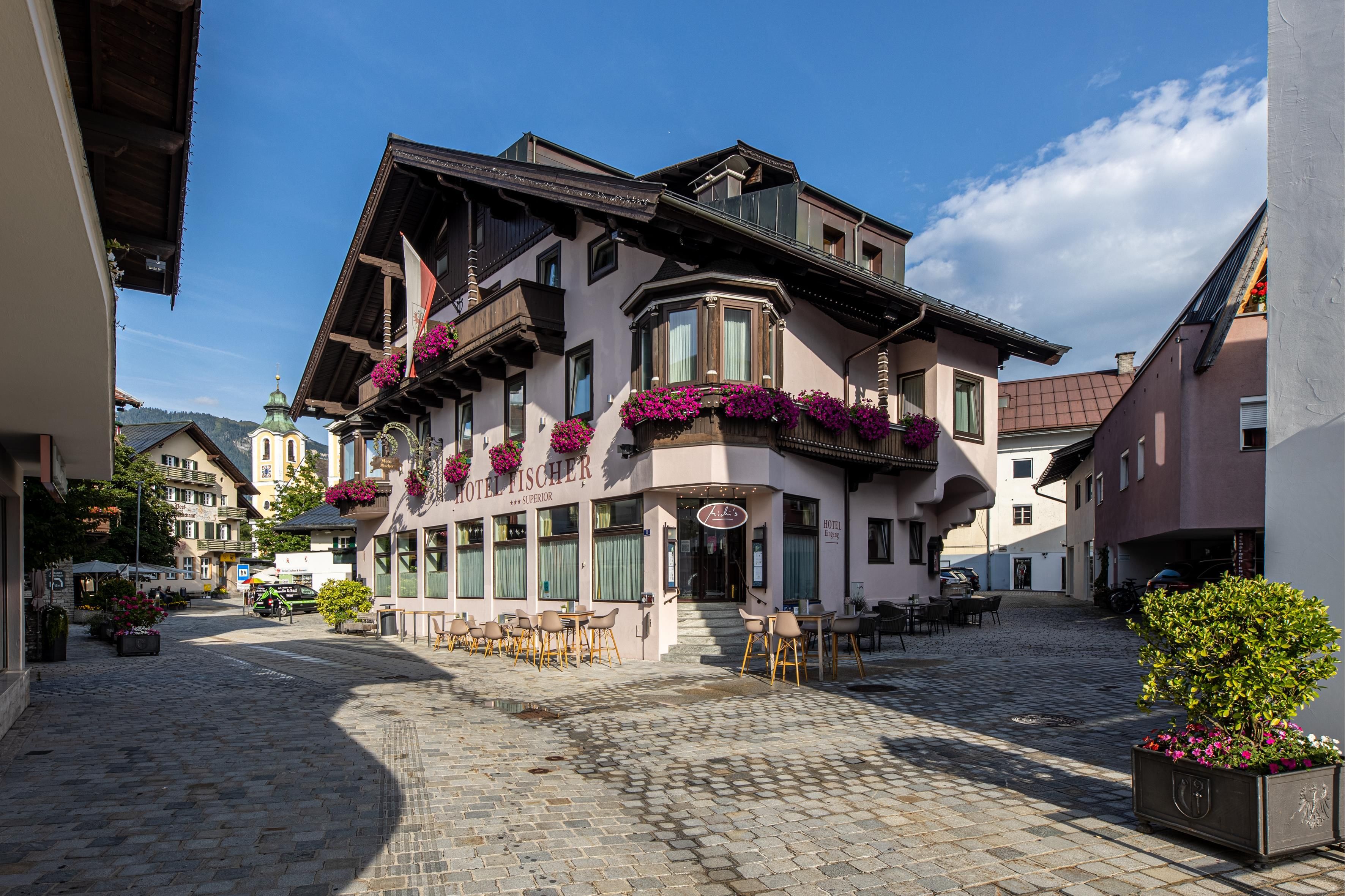 A charming building with flowers in the windows stands on a quiet street. The cobblestone area and the surrounding houses give the scene a picturesque character.