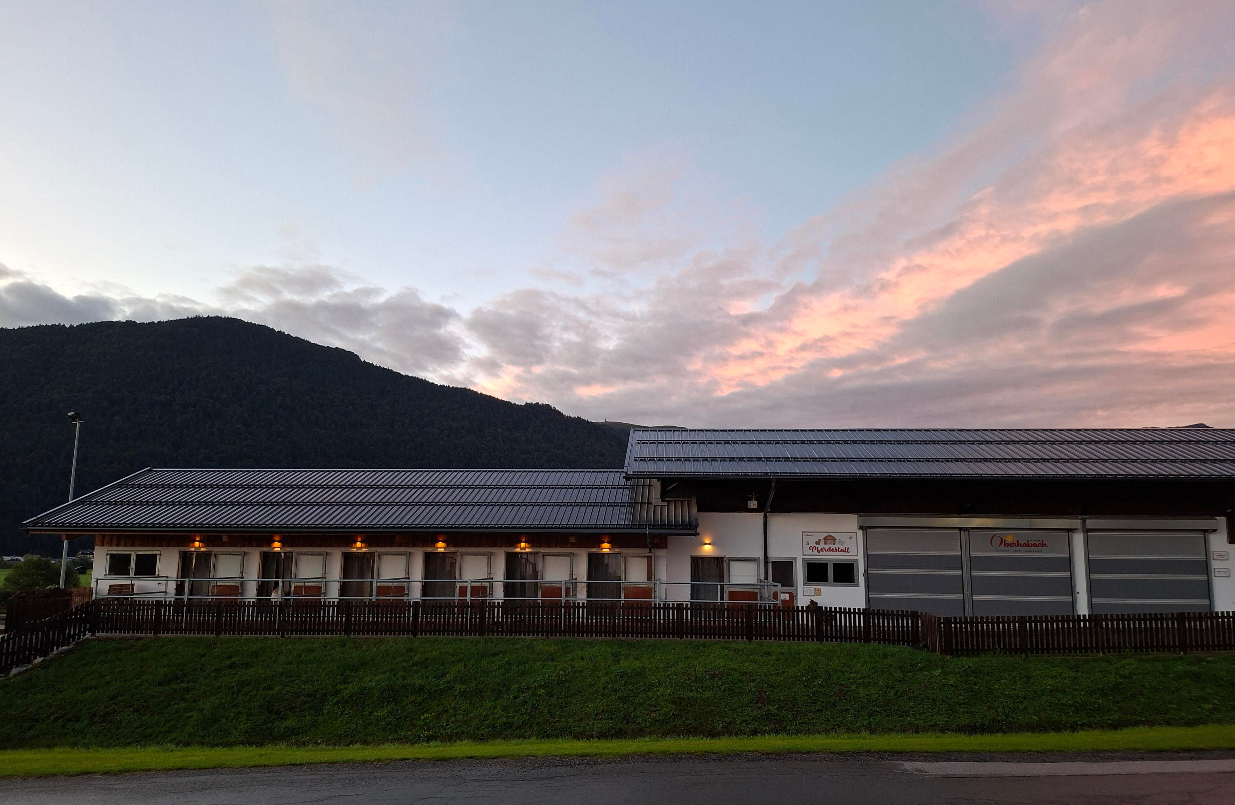 A modern building with a large window front and a garage. In the background, gentle hills and a colorful sky can be seen.