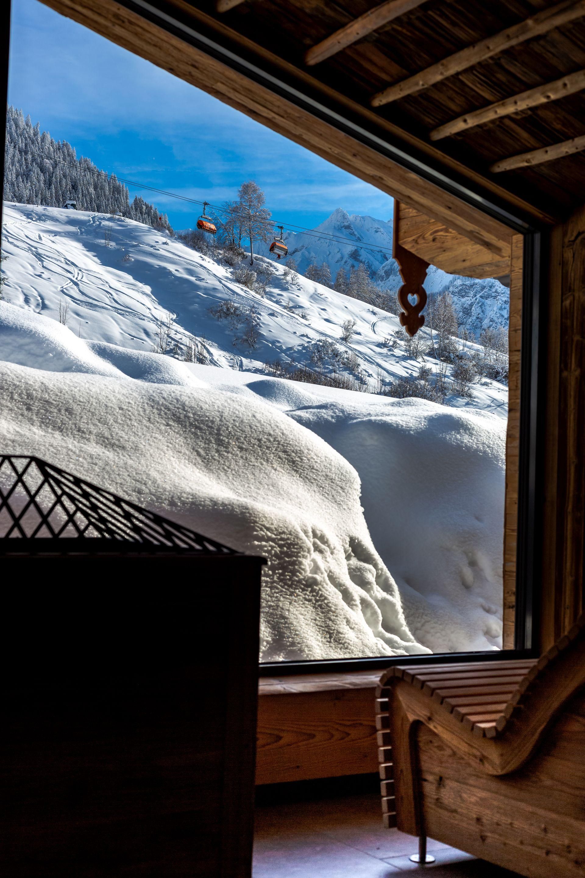A beautiful view from a window of snowy mountains and blue sky. The room has rustic wooden details and feels inviting.