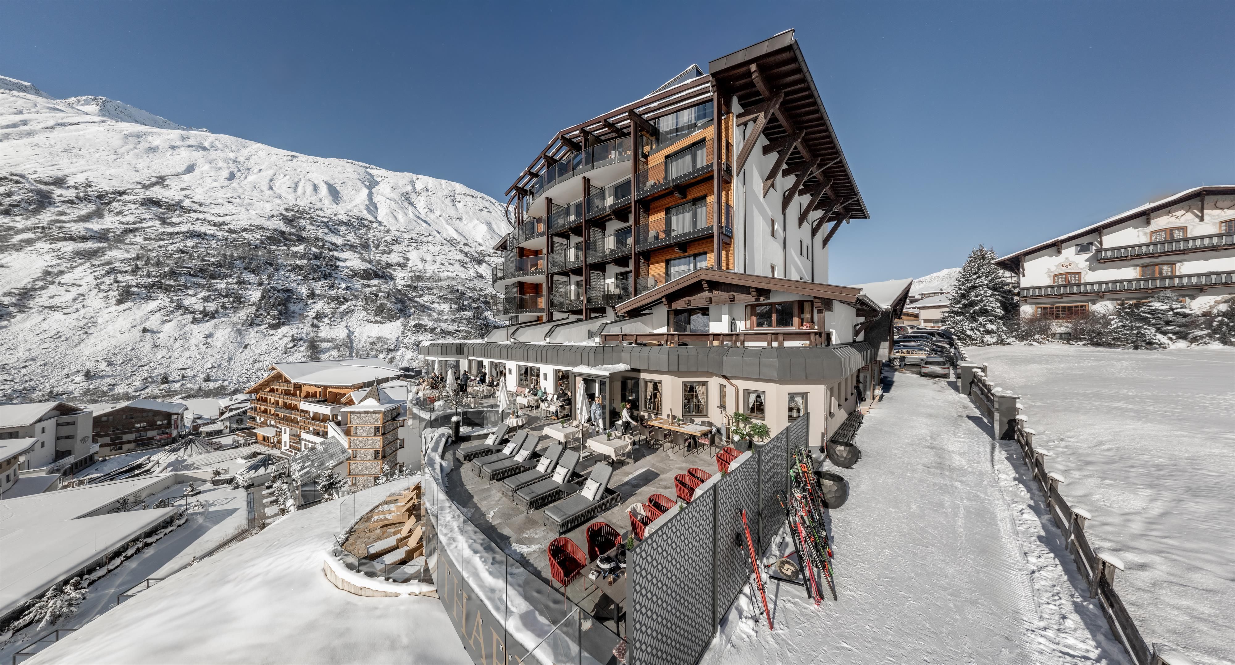 A modern hotel in a snowy mountain landscape. Clear blue skies and cozy loungers on the terrace invite you to relax.