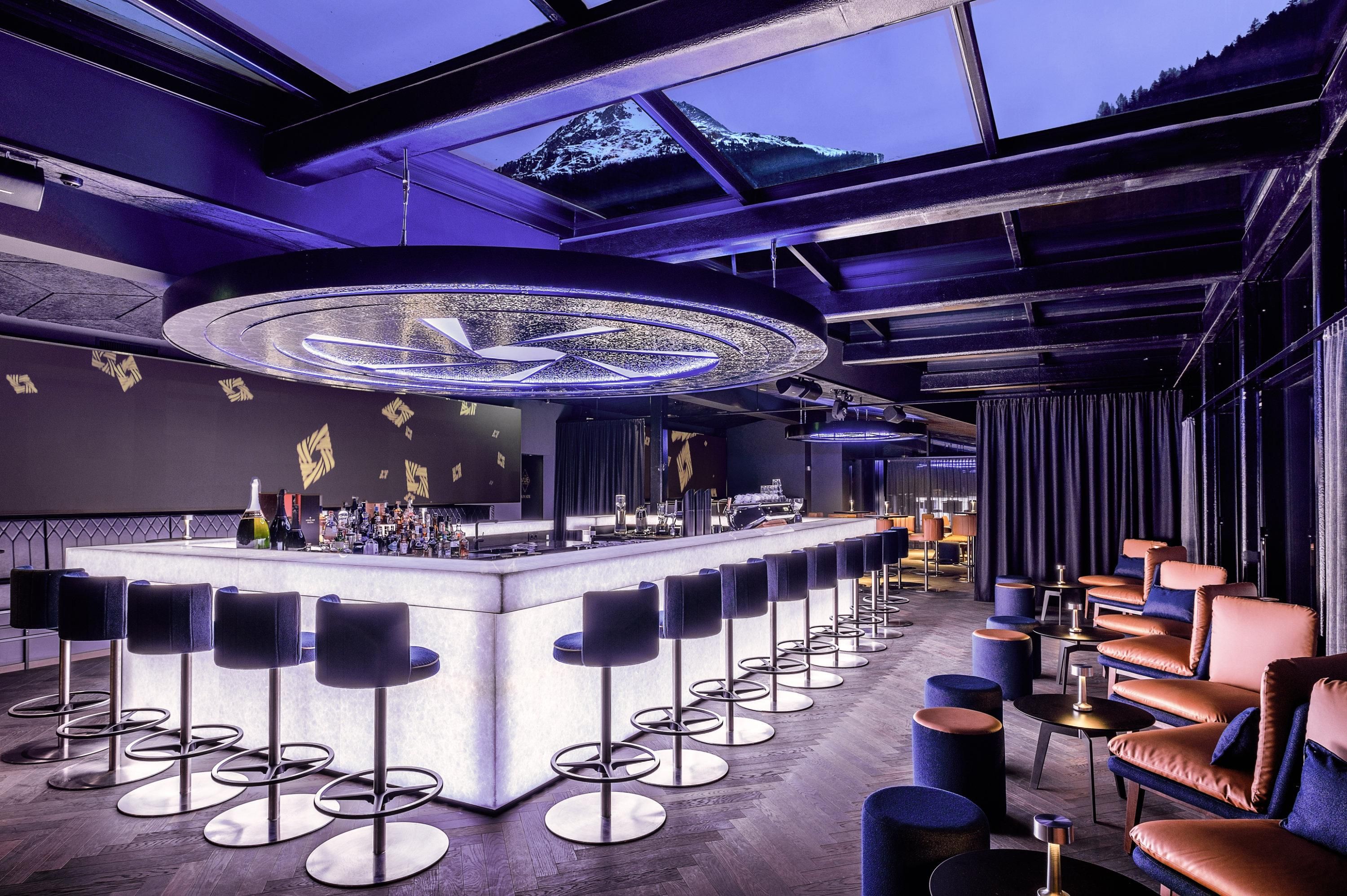 A modern bar with elegant chairs and a glowing counter. Large windows offer a view of the mountains and create a stylish ambiance.