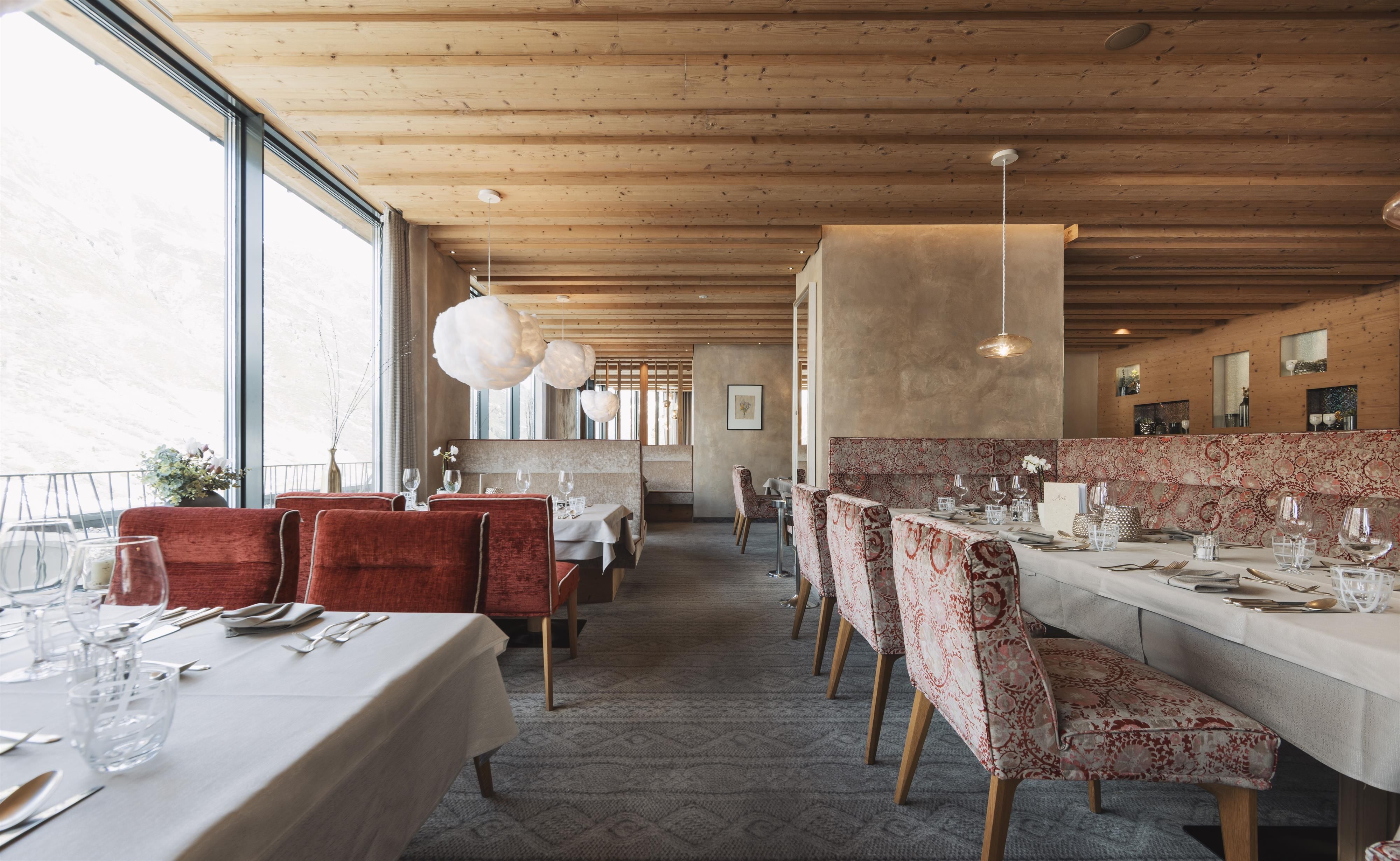 An elegant restaurant with a wooden ceiling and large windows. The tables are set in a friendly manner, and the furniture is stylishly arranged.