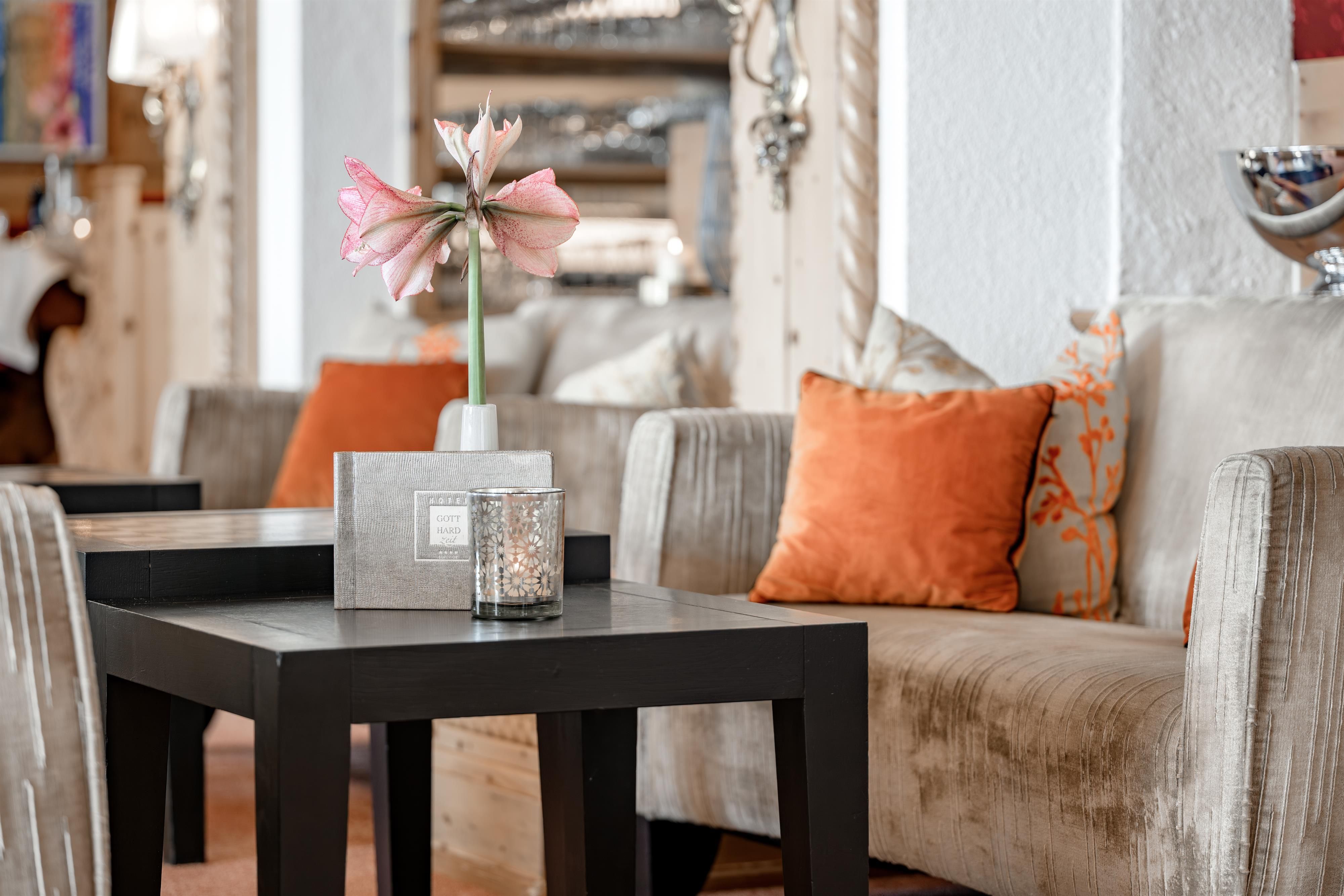 An elegant living area with comfortable sofas and colorful cushions. On a black table stands a vase with a beautiful flower.