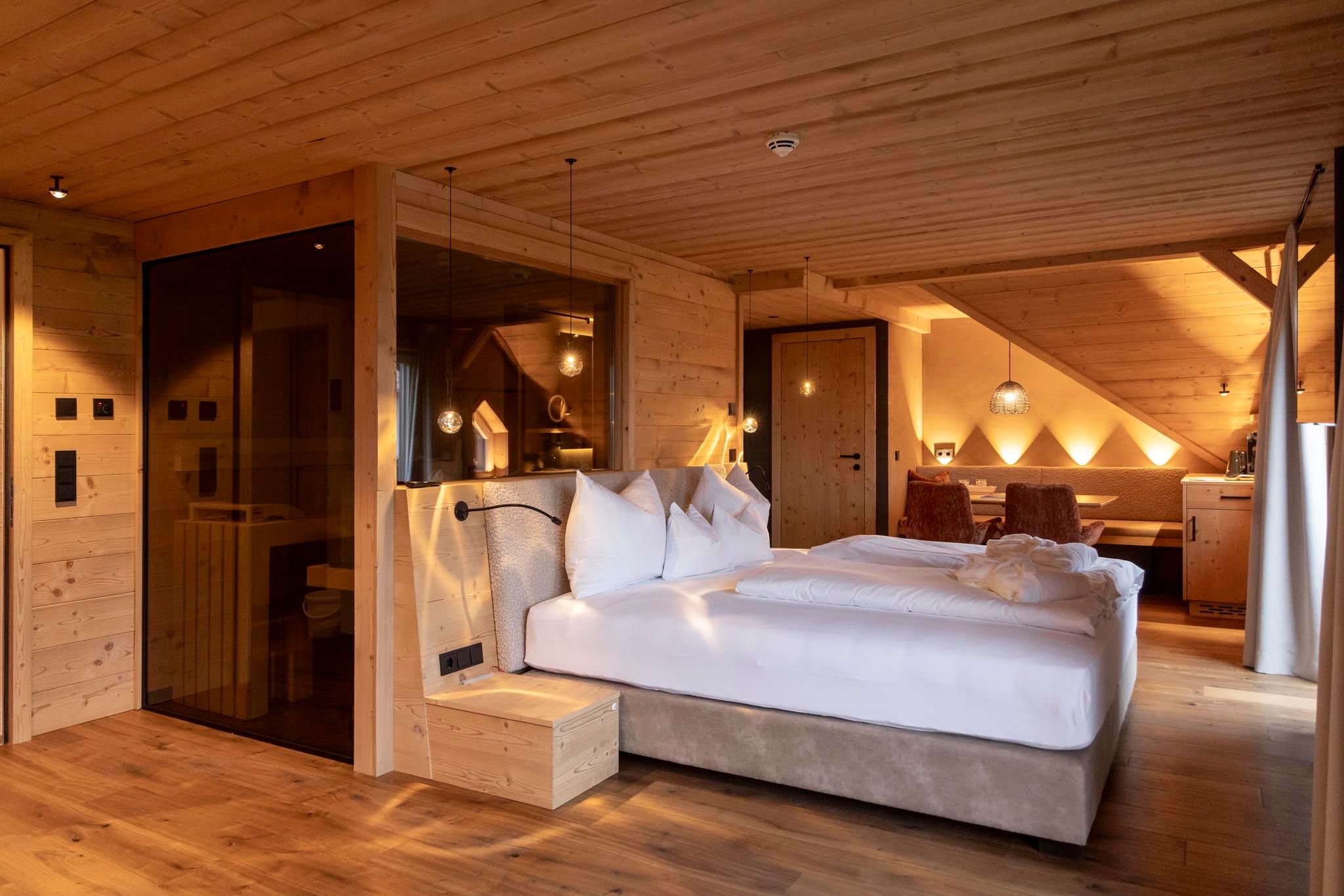 A modern bedroom with wood decor and a cozy bed. The room features an adjoining glass shower and a warm, inviting atmosphere.