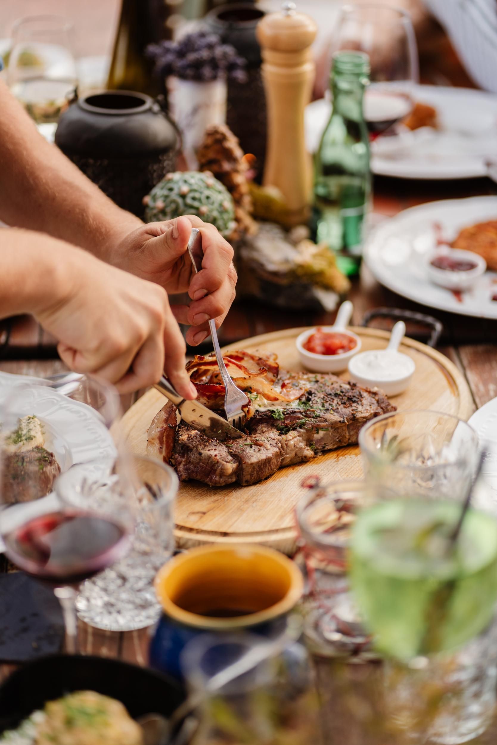 A delicious steak is served on a rustic table. Surrounding the steak are various drinks and side dishes.