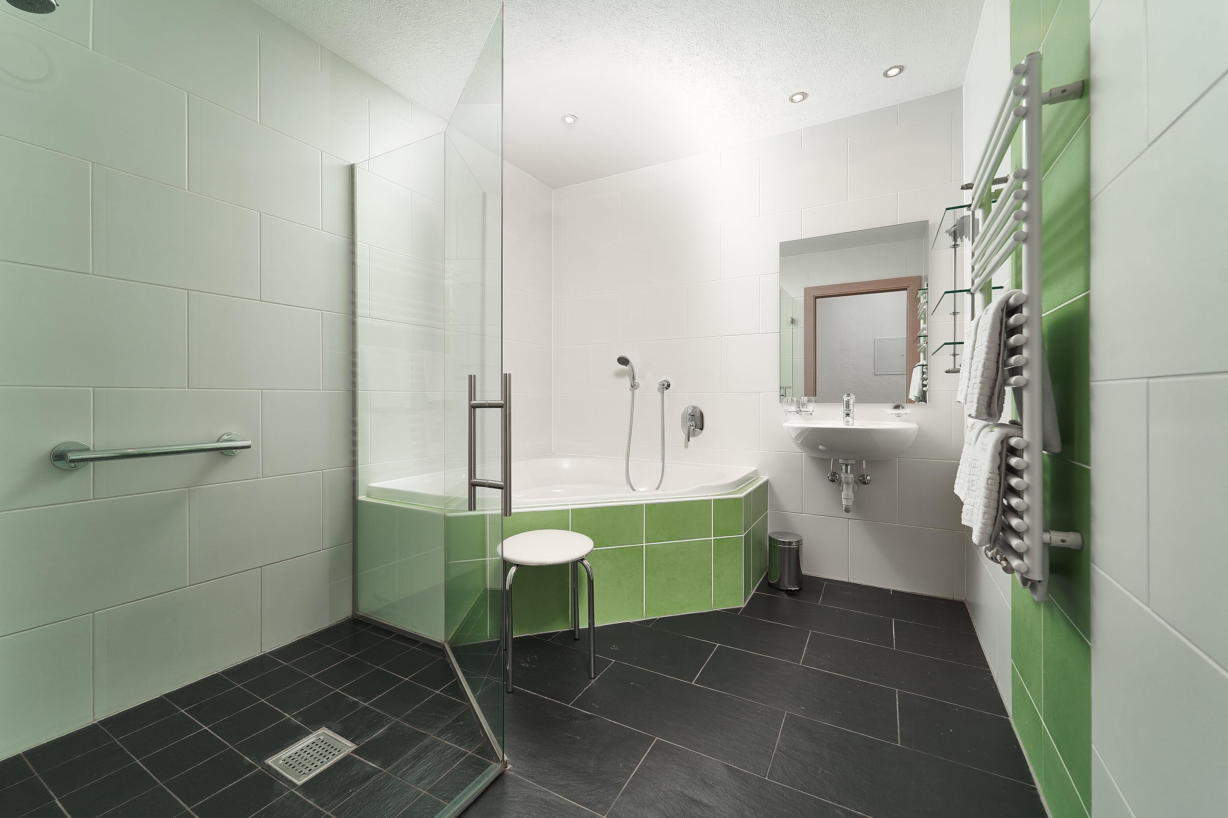 A modern bathroom with a shower and a freestanding bathtub. The walls are designed in white and green, with gray tiles on the floor.