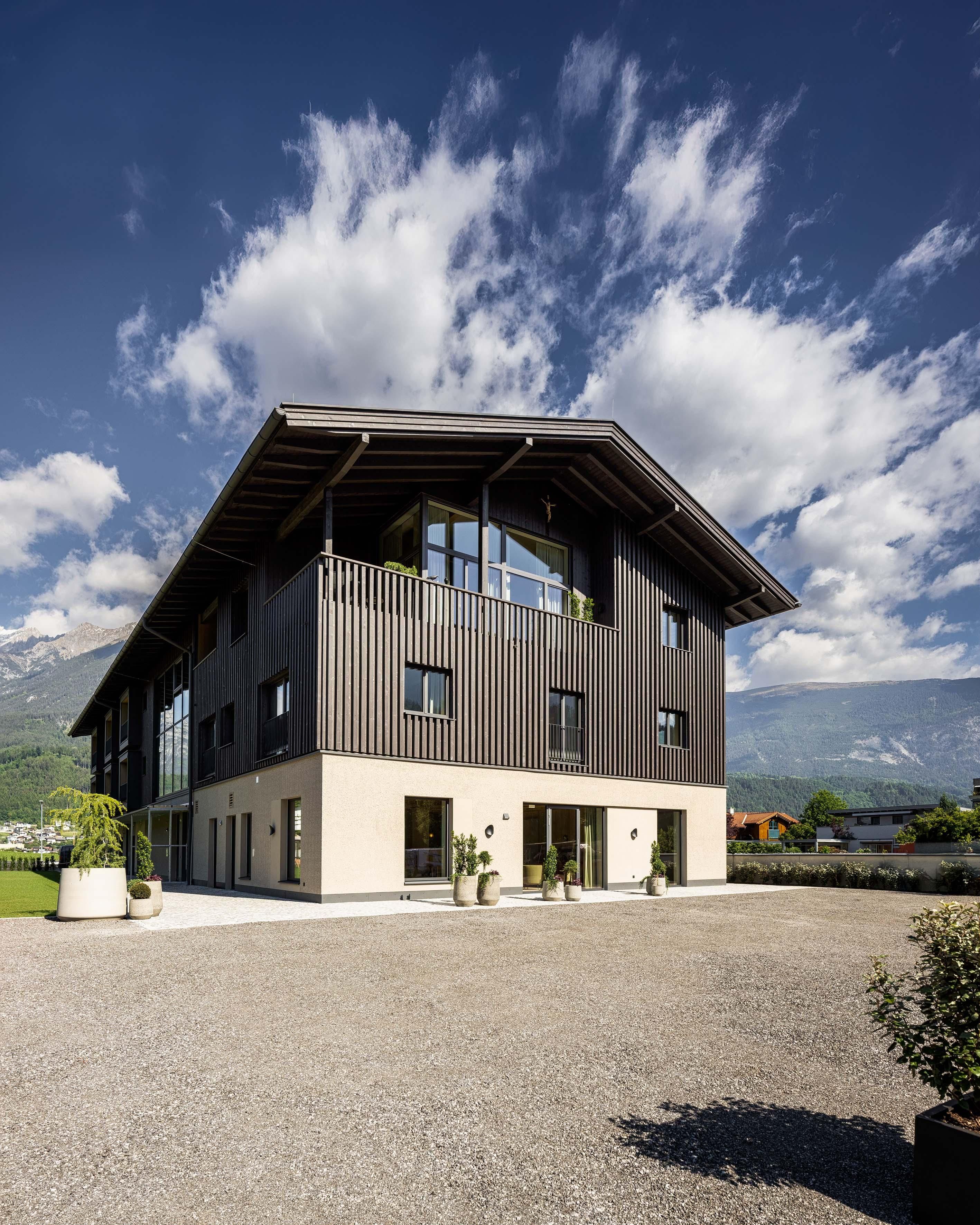 A modern building with wooden cladding and large windows. The sky is blue with a few clouds and there is plenty of space around the house.