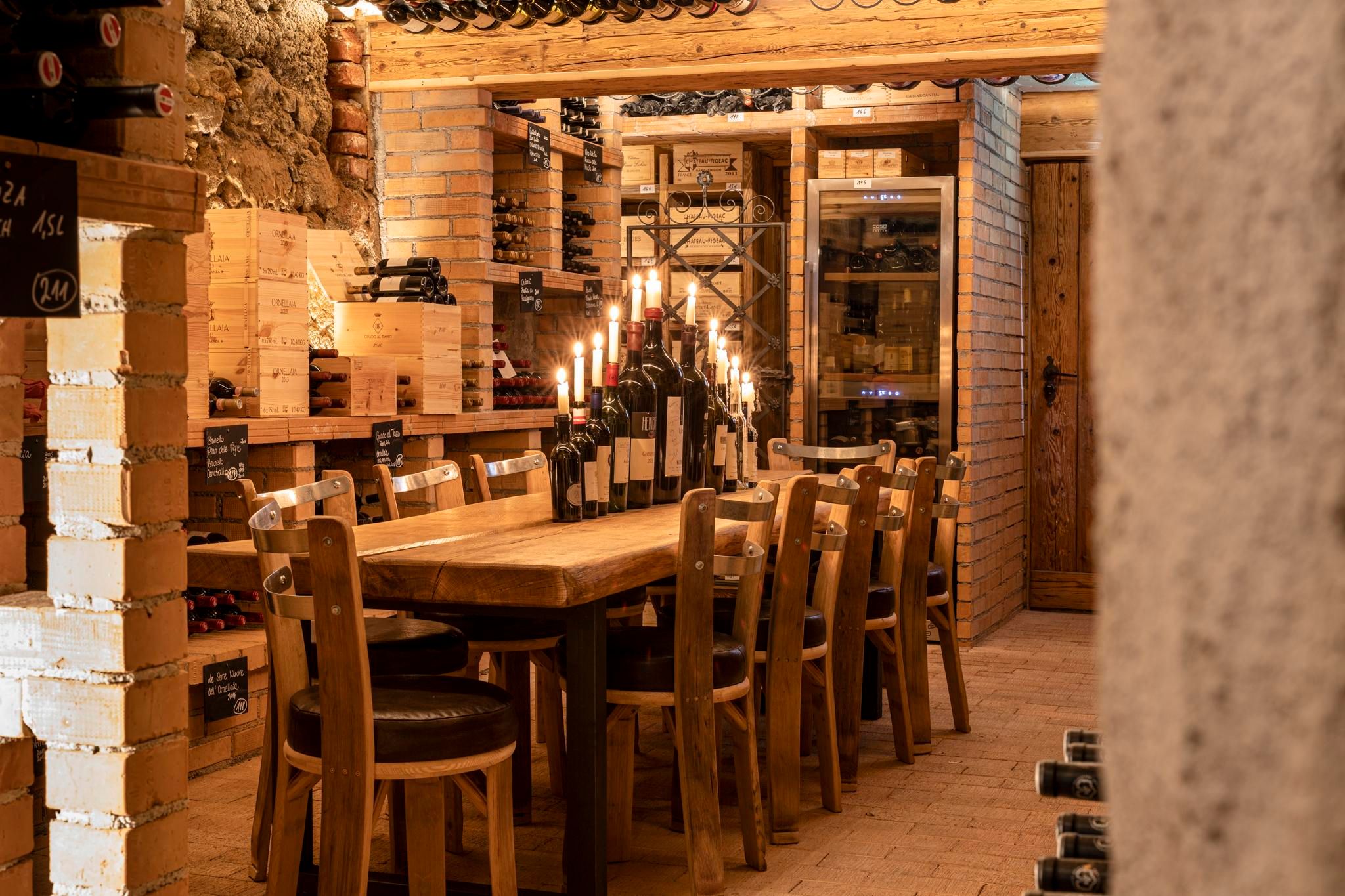 A cozy wine cellar with a large wooden table and chairs. Shelves full of wine bottles and candlelight create an inviting atmosphere.