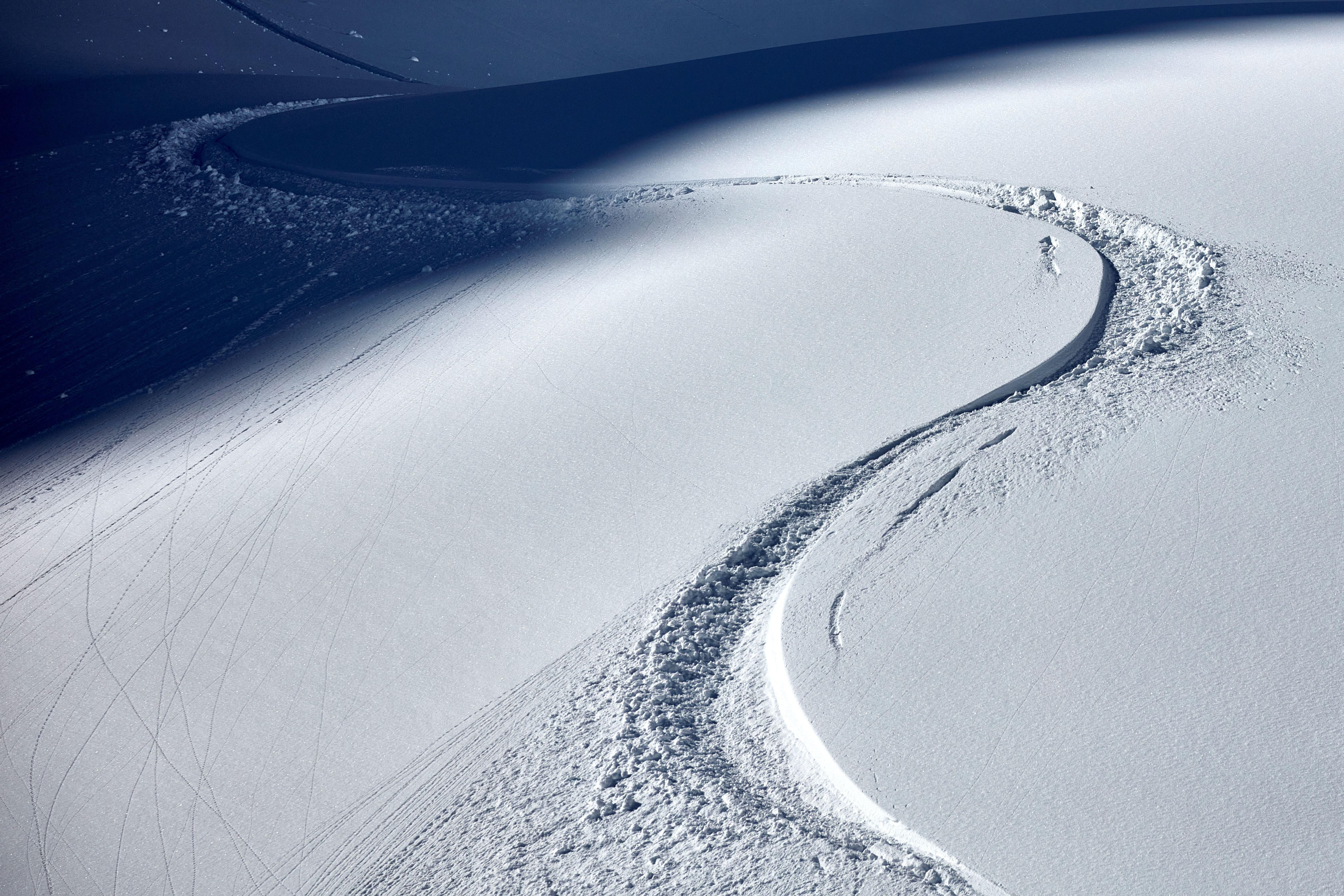 A snowy slope with clear tracks in the snow. The gentle curves show the movement of a skier.