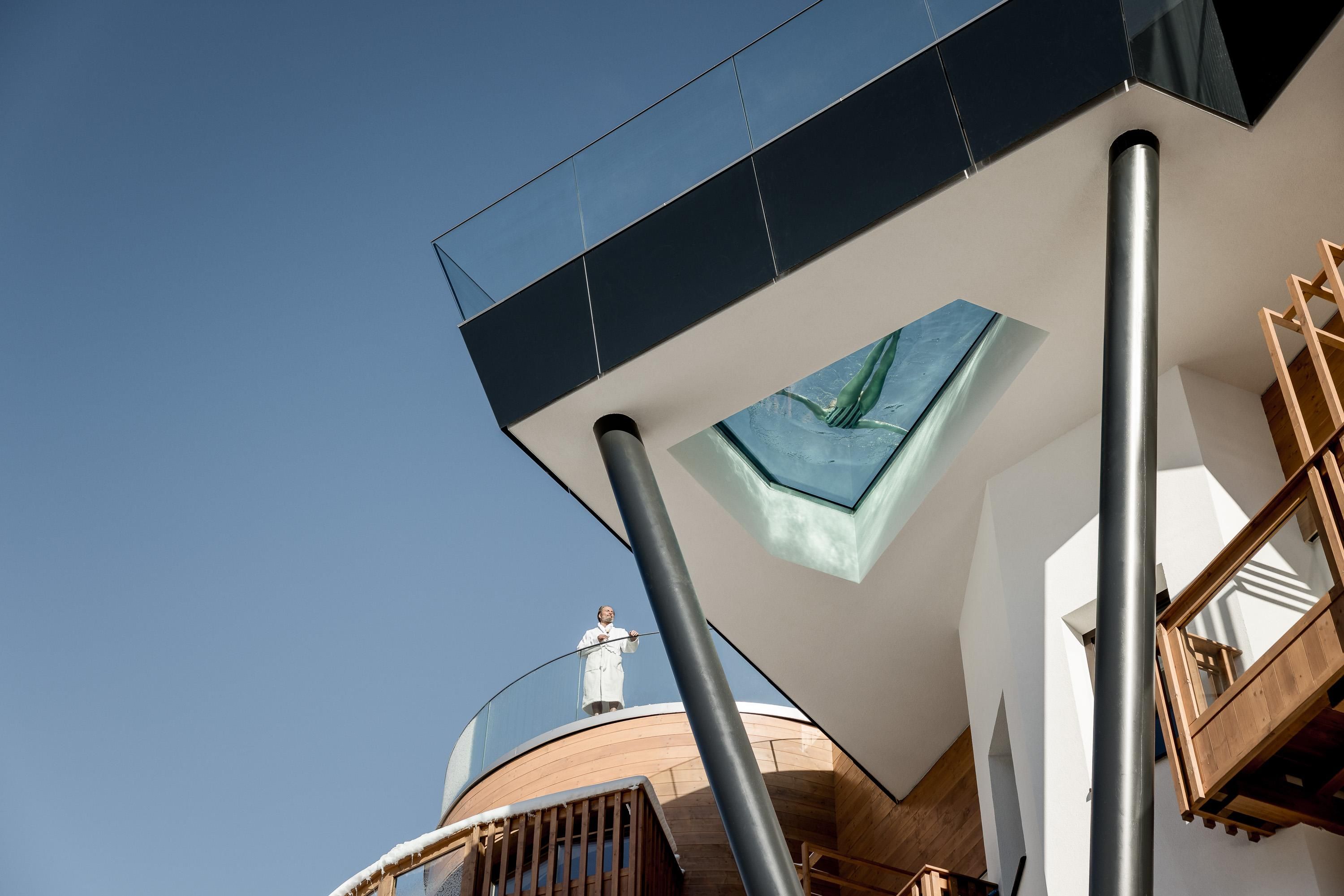 A modern building with a rectangular upper floor and a glass roof. The architecture is minimalist and reflects a clear blue sky.