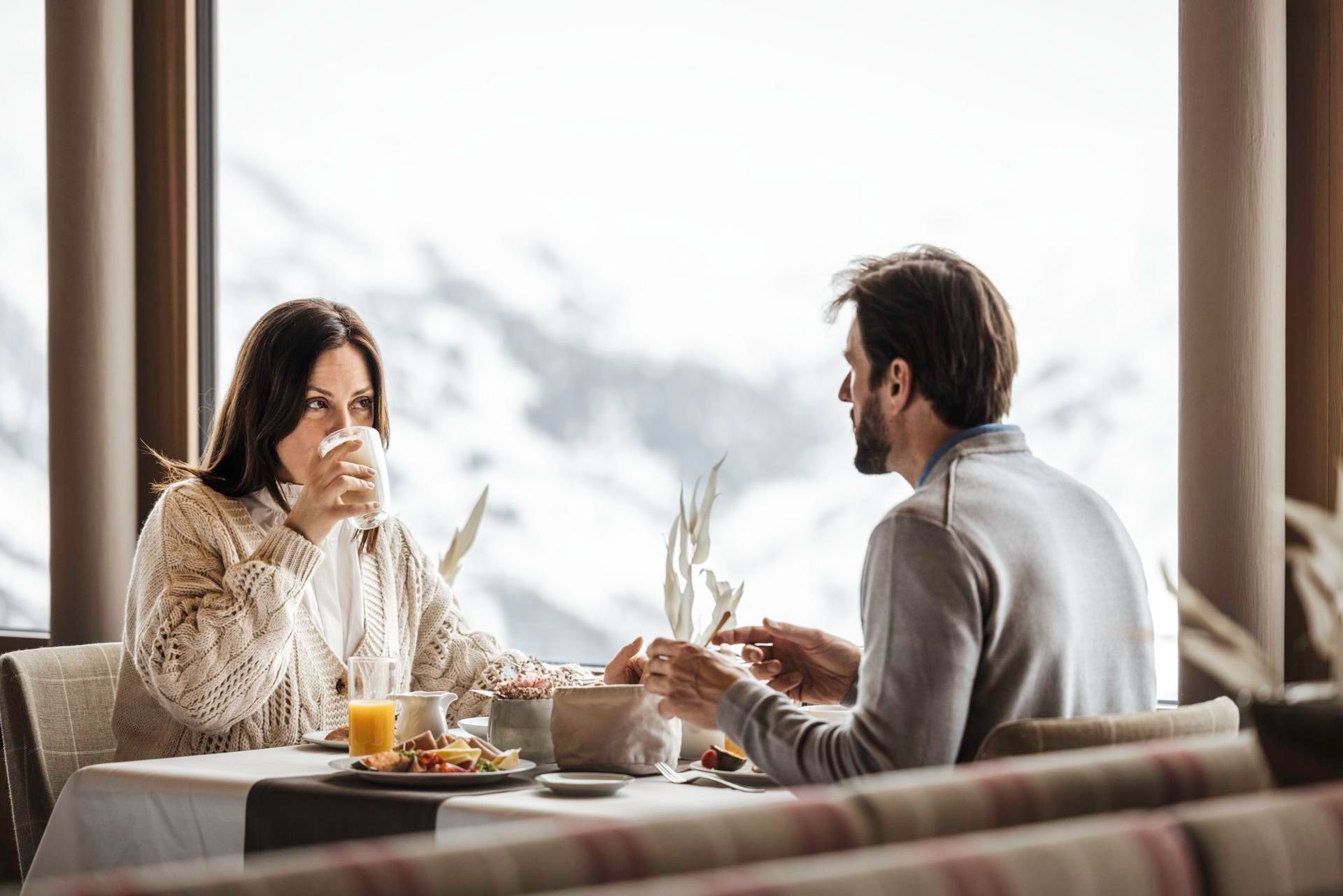 A couple is sitting at a table enjoying breakfast with a view of the mountains. The atmosphere is cozy and inviting.