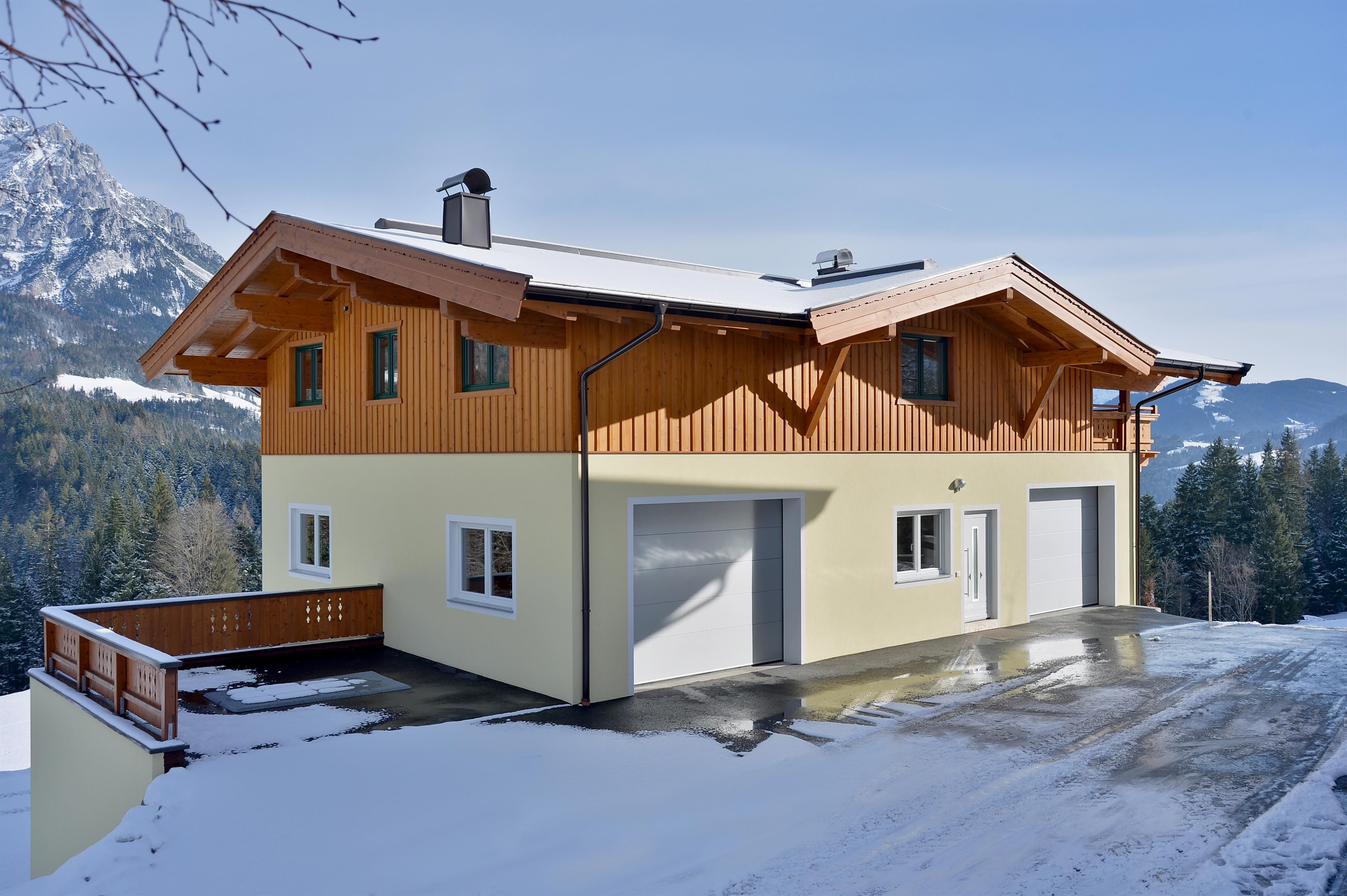 A modern house in a snow-covered landscape. In the background, there are mountains and a clear sky.