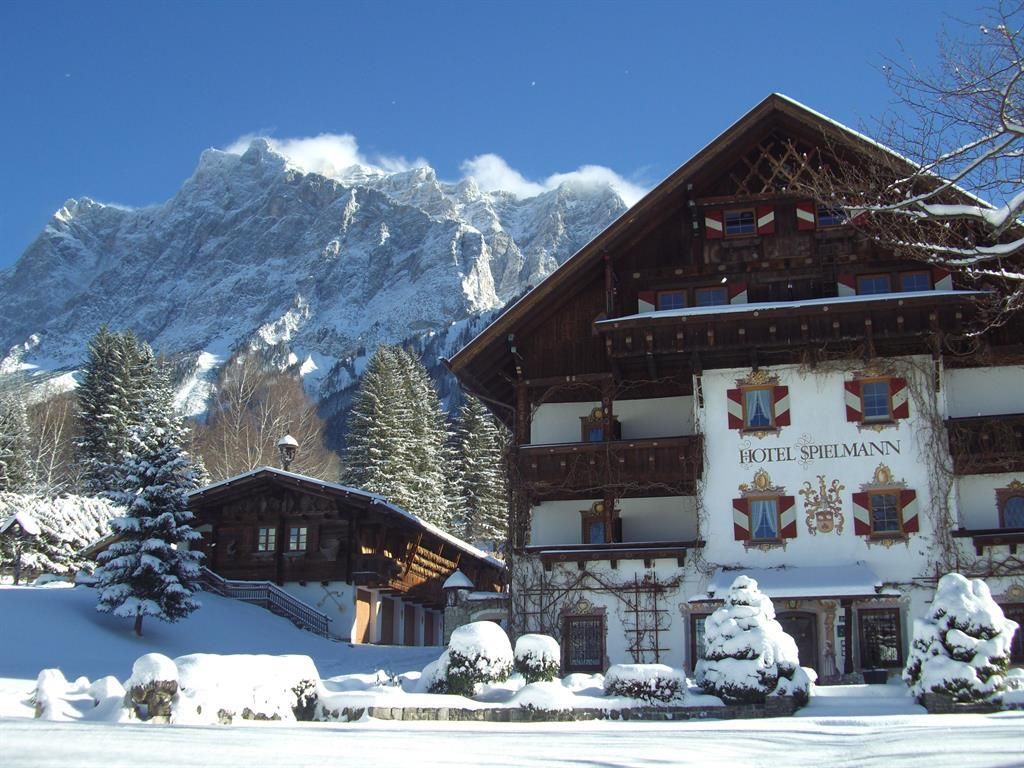A picturesque hotel in the snow with majestic mountains in the background. The clear blue sky complements the winter landscape.