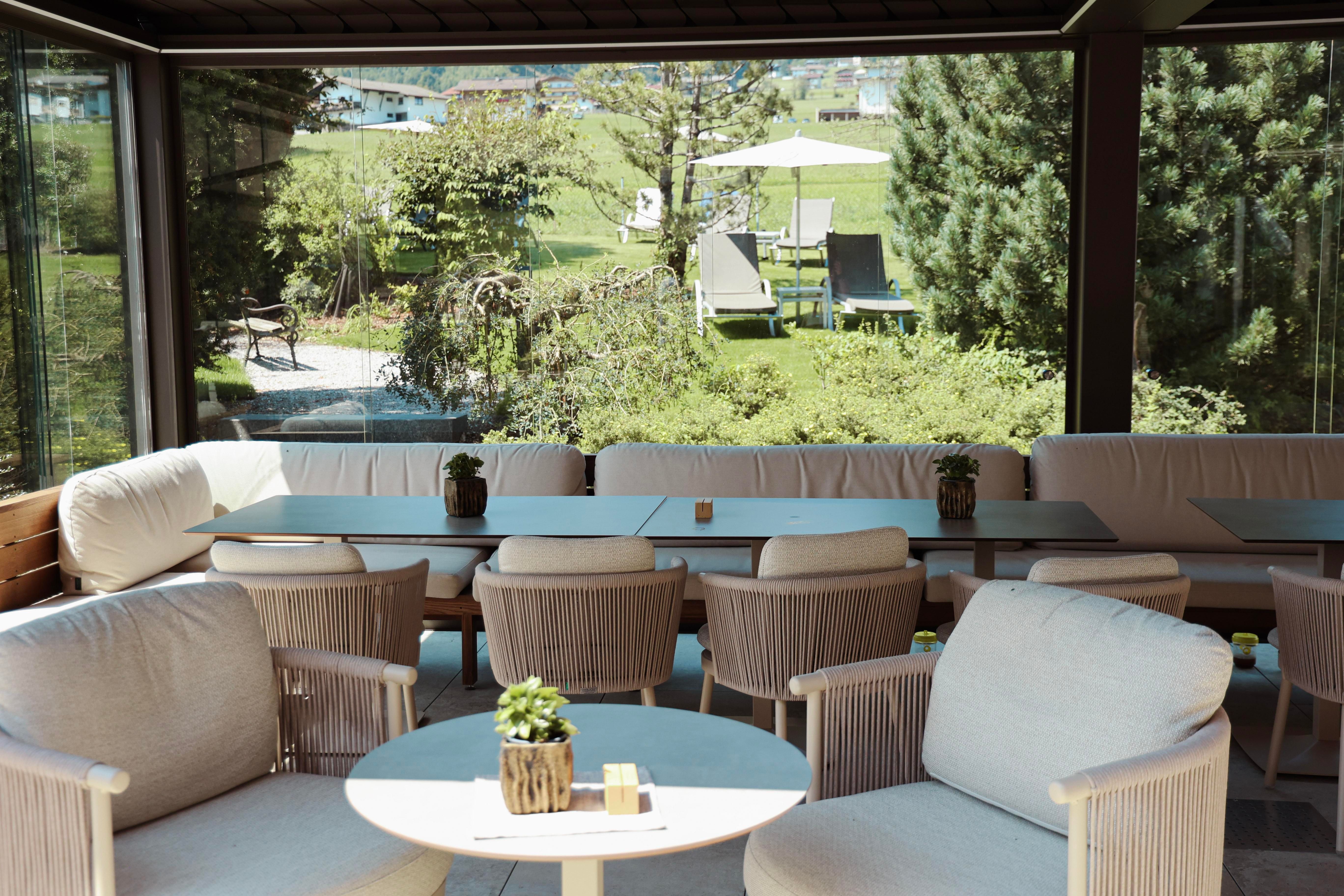 A cozy interior with comfortable armchairs and tables. In the background, a green garden landscape can be seen.