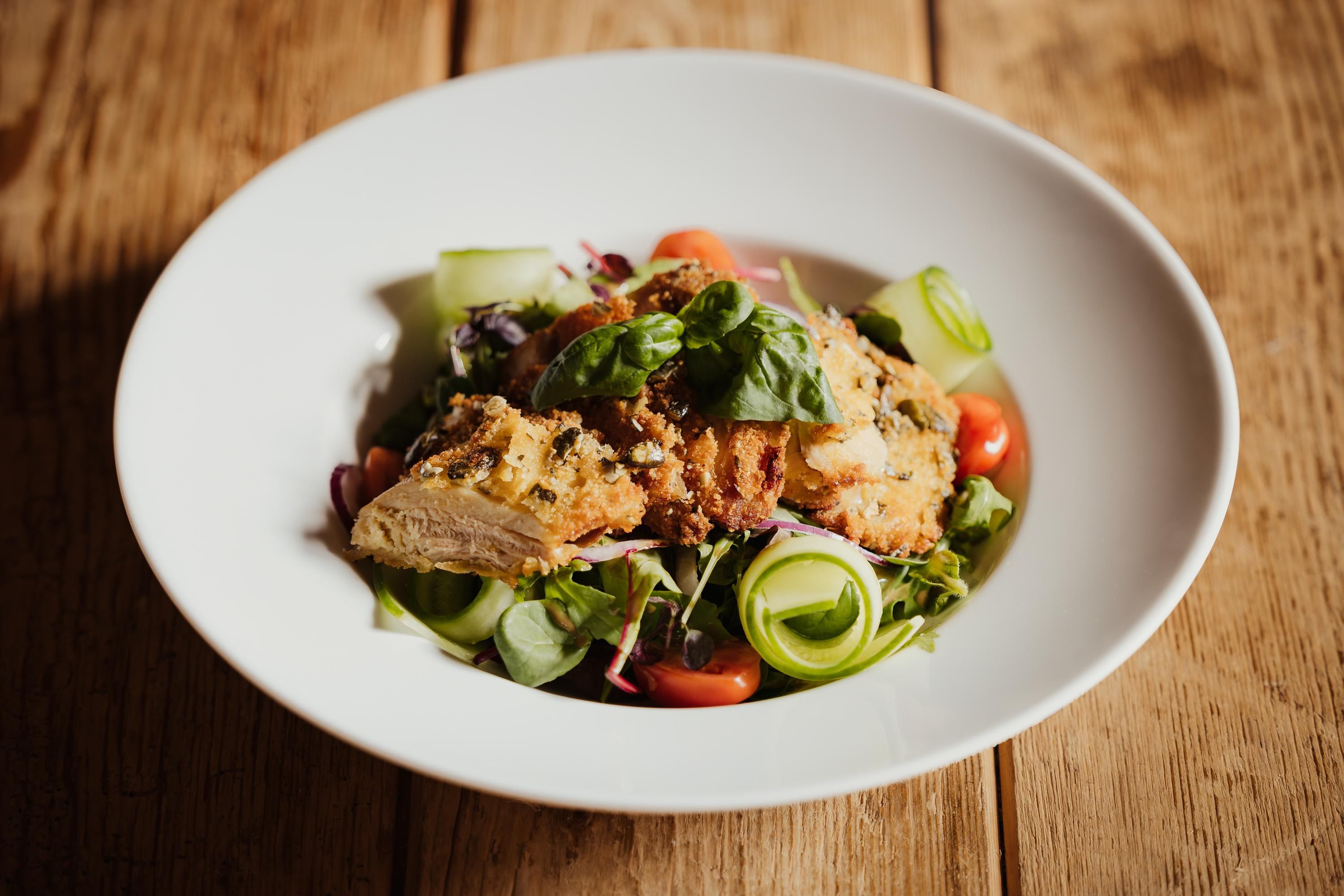 A delicious plate with crispy chicken and fresh vegetables. Accompanied by a colorful salad with tomatoes and herbs.