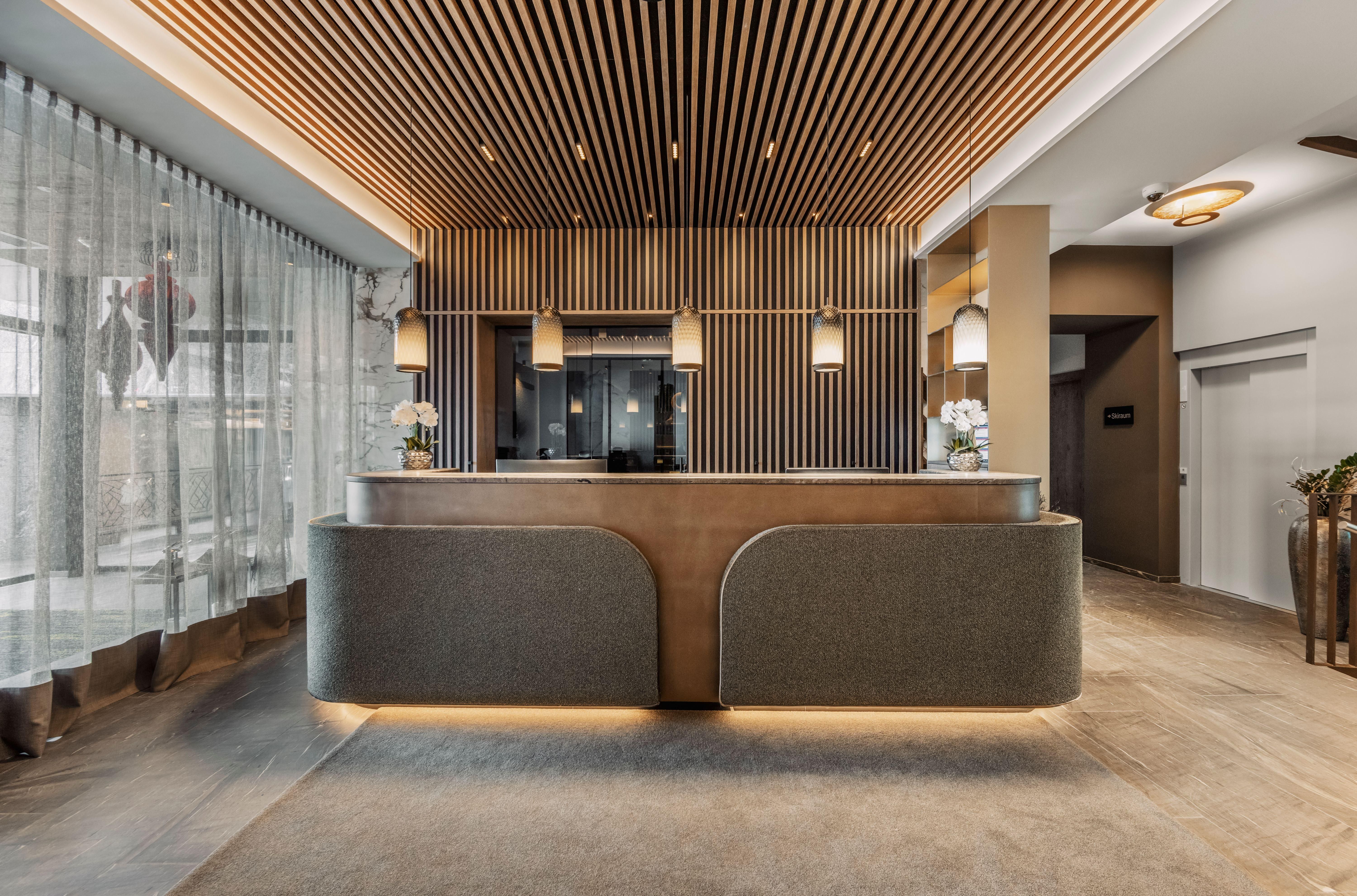 An elegant reception with stylish wood design and modern lamps. In the background, large windows with curtains can be seen, creating a bright atmosphere.