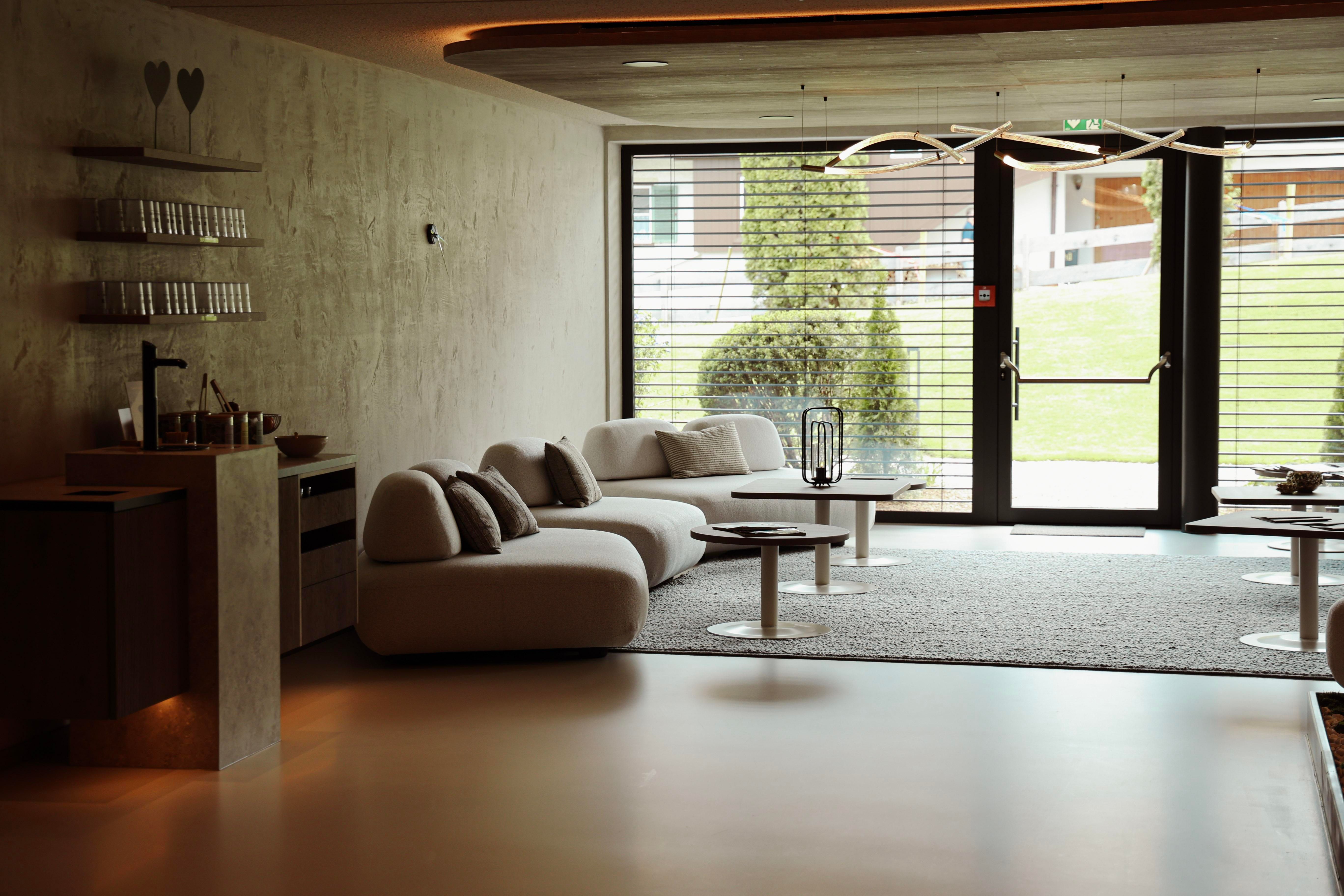 An elegant room with a modern sofa and a large window. The room is bright and friendly, with a carpet and a minimally designed bar.