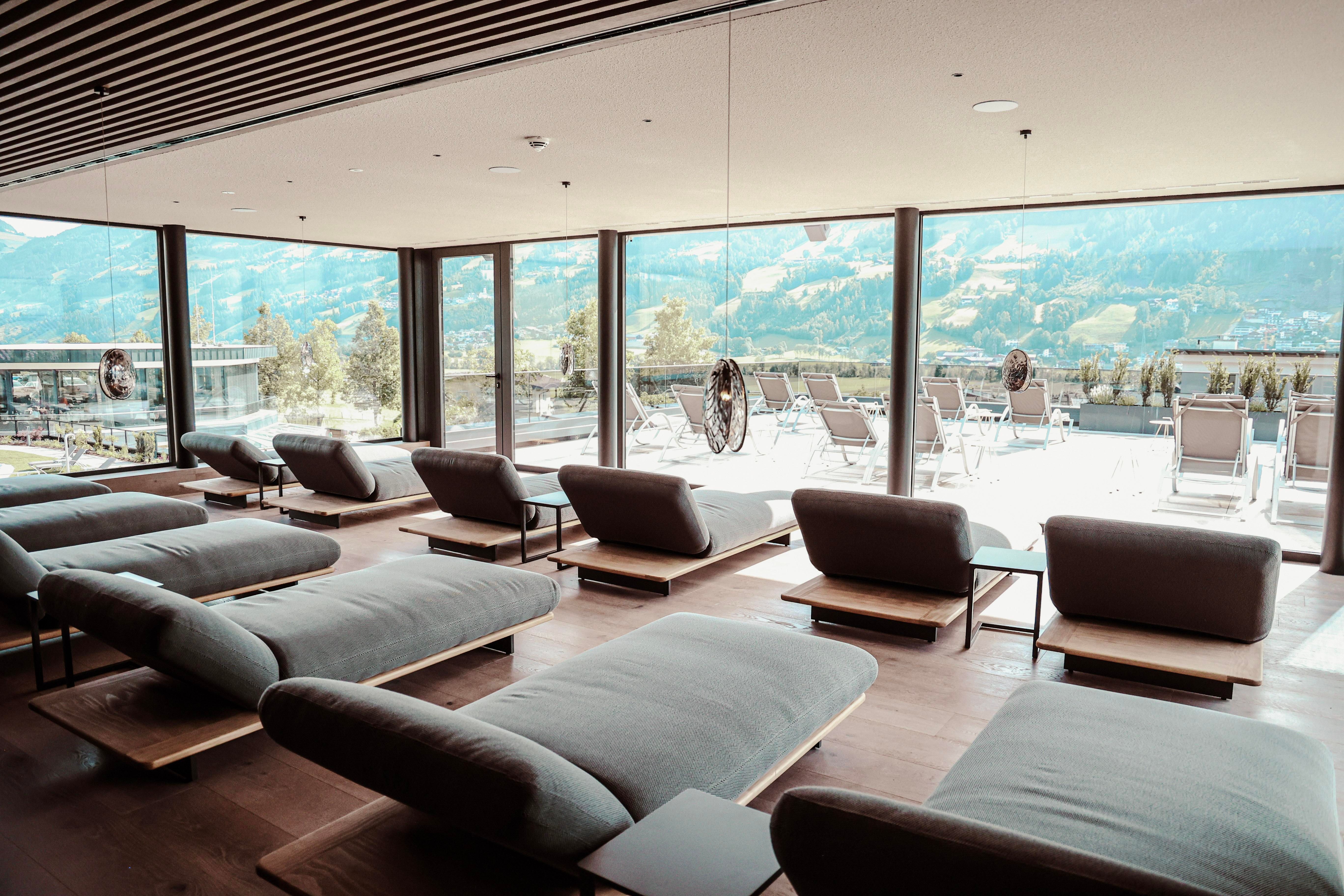 A modern relaxation room with comfortable loungers and large windows. The view showcases a picturesque landscape with mountains in the background.