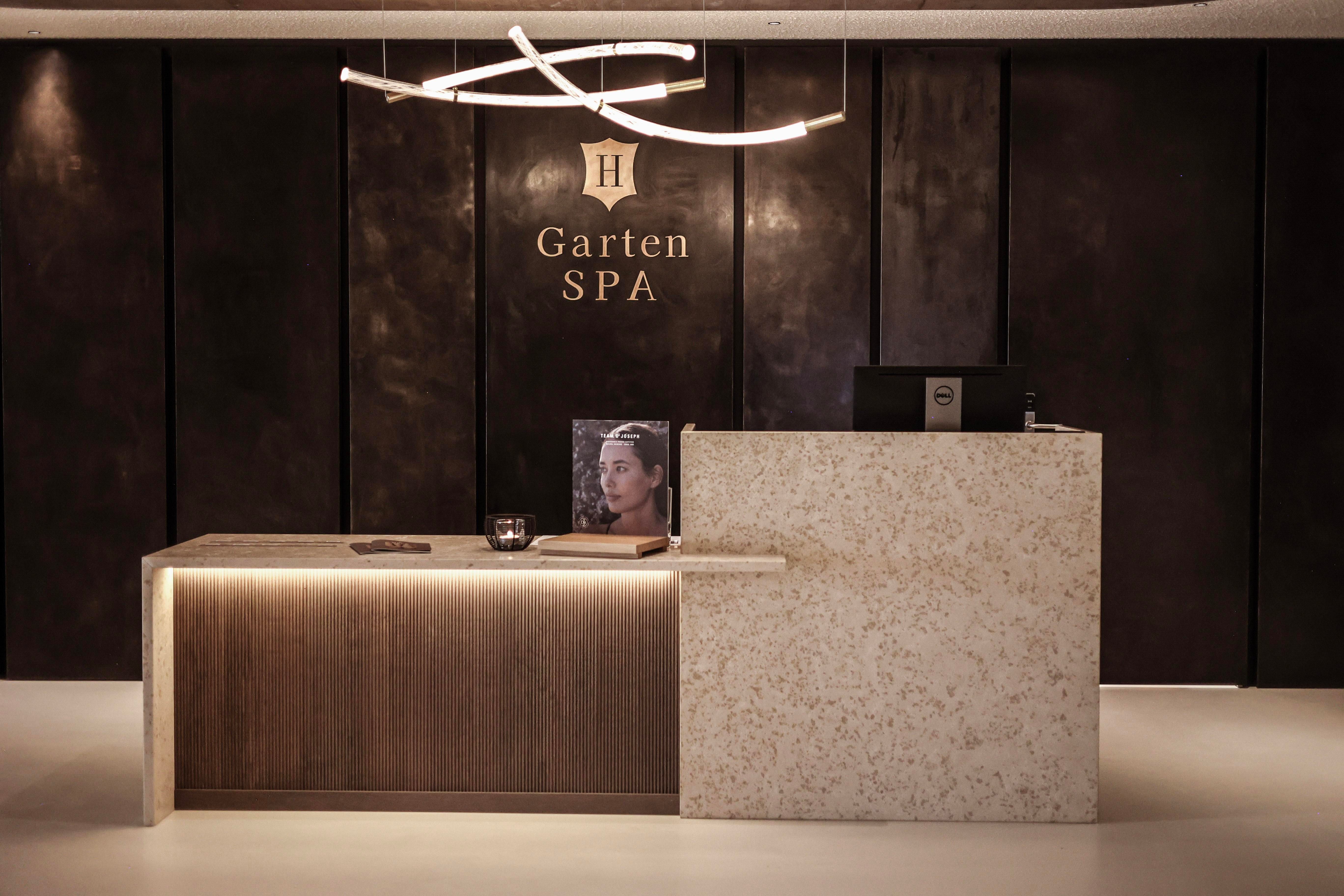 A modern reception area of the garden SPA with an elegant counter made of wood and stone. The walls are dark and sophisticated, and soft lighting creates a relaxed atmosphere.
