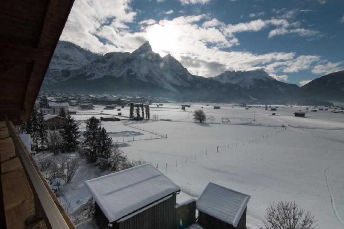 A winter landscape with snow-covered fields and mountains in the background. The sky is partly cloudy, allowing a gentle light to shine through.