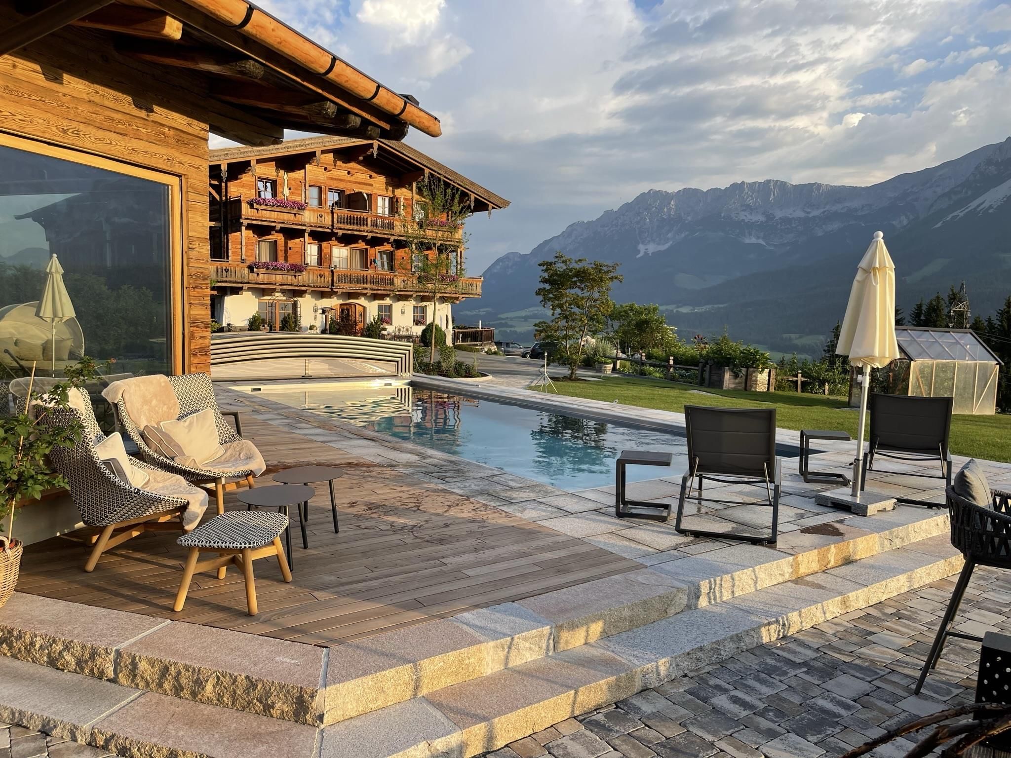 A luxurious terrace with a pool and comfortable seating options. In the background, majestic mountains and a picturesque landscape can be seen.