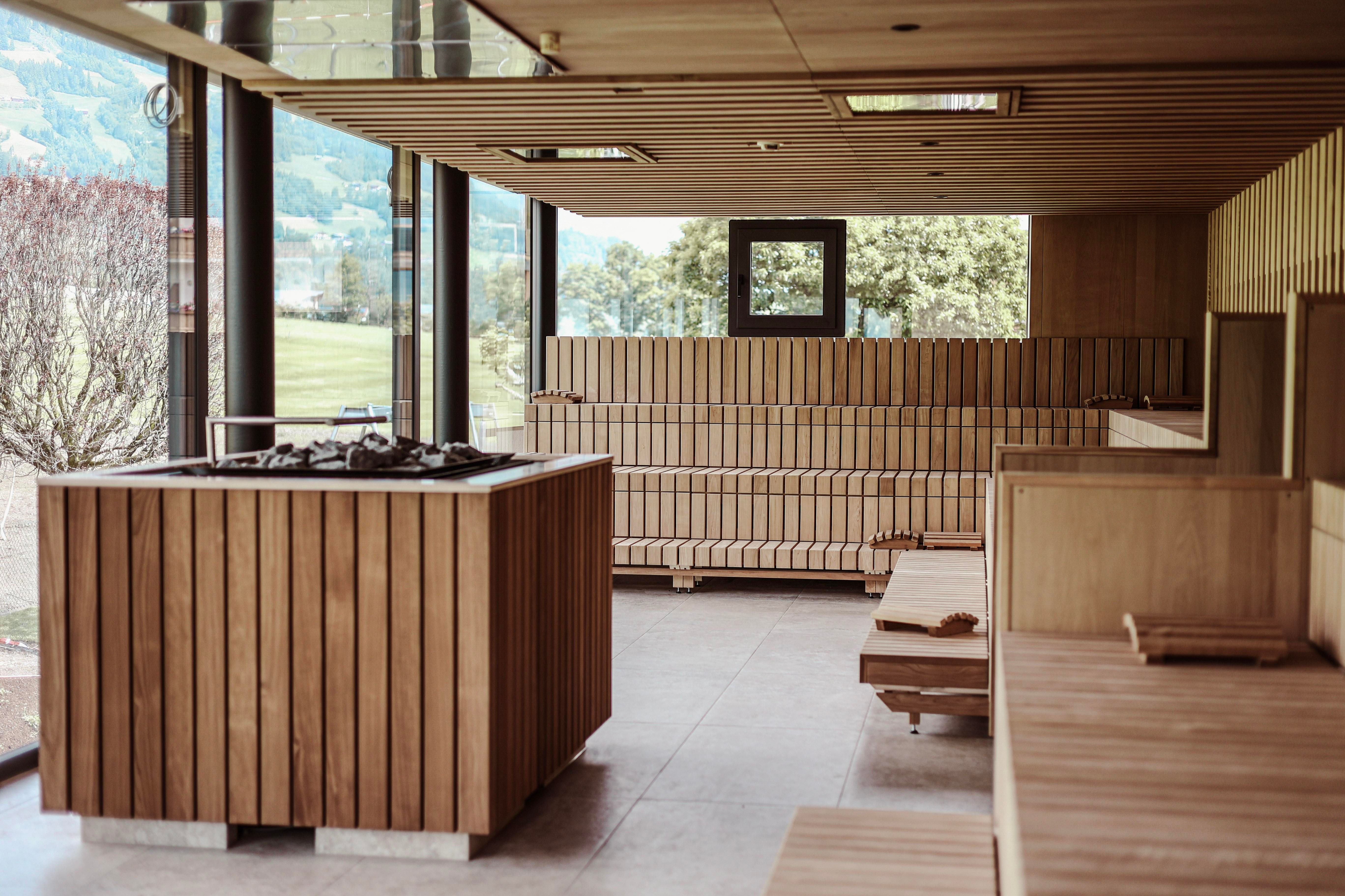 A modern wellness area with wooden paneling and large windows. In the center is a sauna stove and cozy wooden loungers.