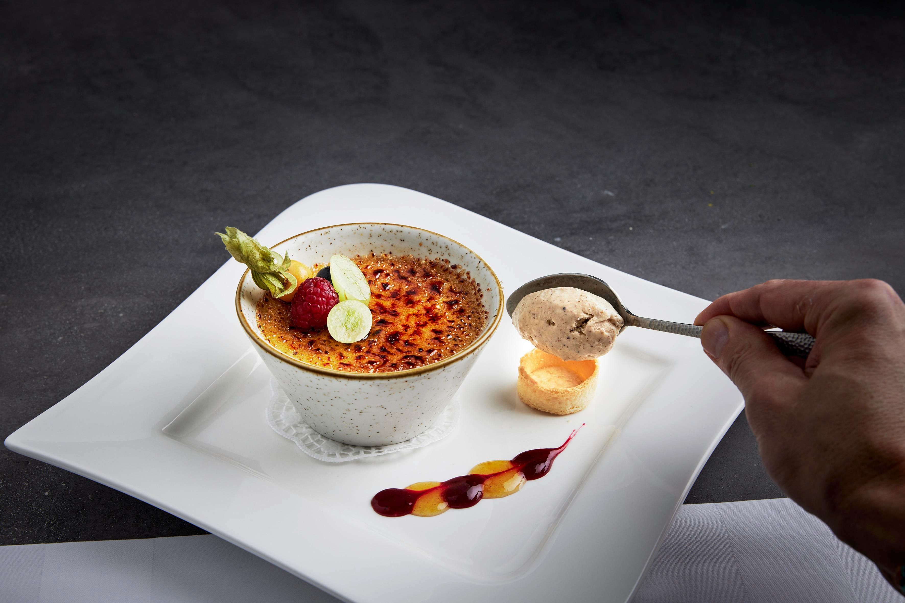 A delicious crème brûlée with a caramelized surface and fresh berries. Next to it lies a small scoop of ice cream on a white plate.